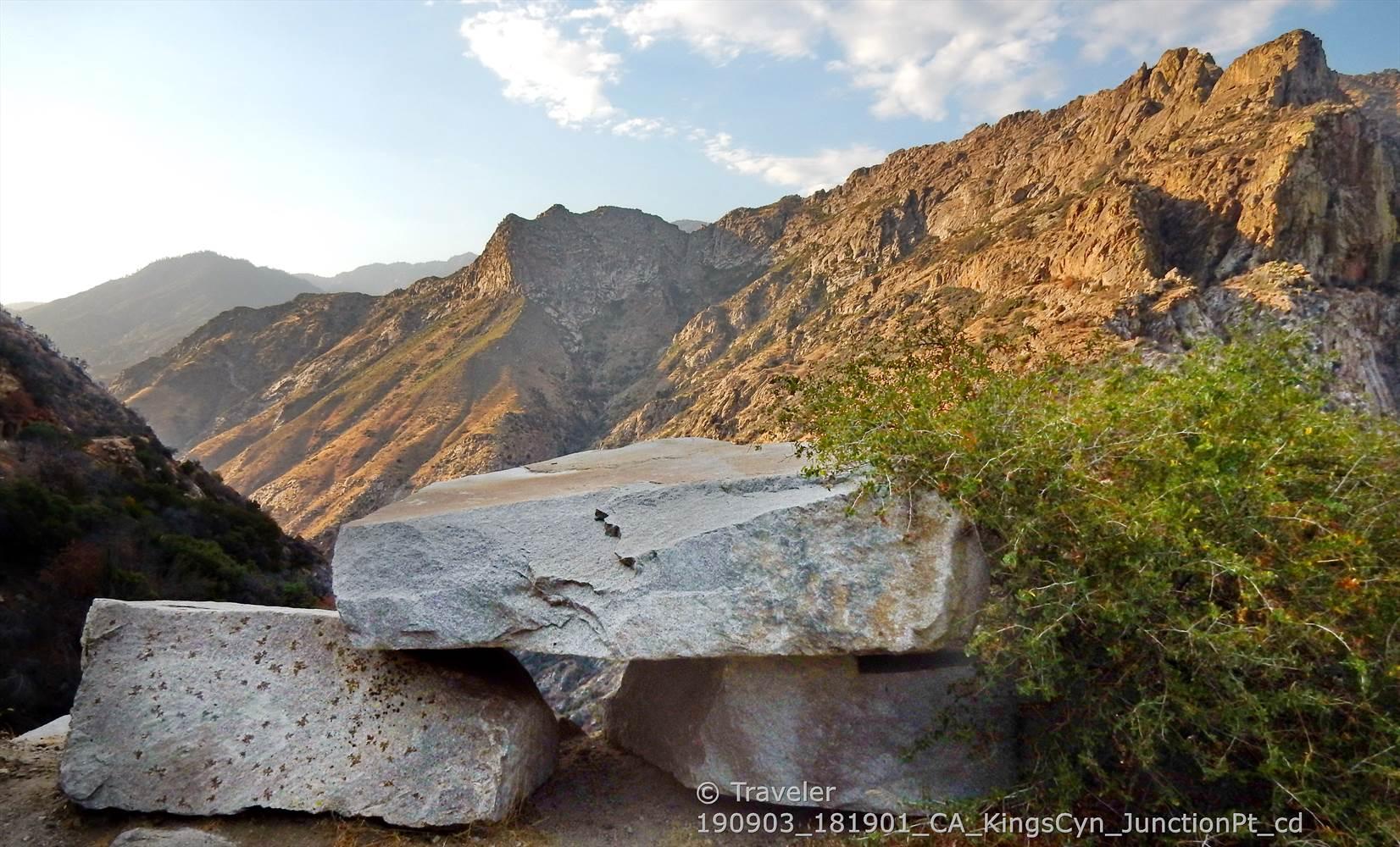 Large cut stone blocks in the foreground, with sunlit mountains and a cloudy sky.