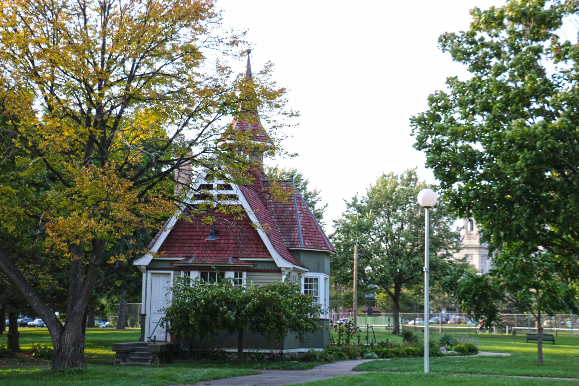 Small, charming building with a red roof nestled among lush green trees.