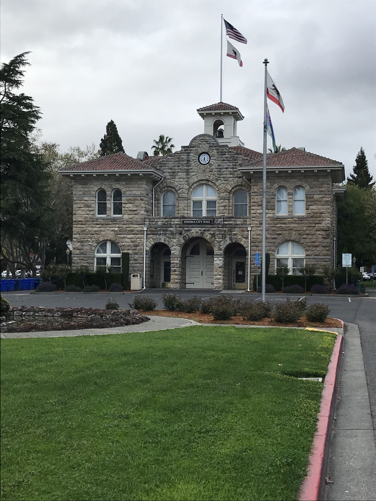 A large stone building with flags flying under an overcast sky. - Vineyard Road in Napa Valley – Sonoma Plaza loop from Sonoma