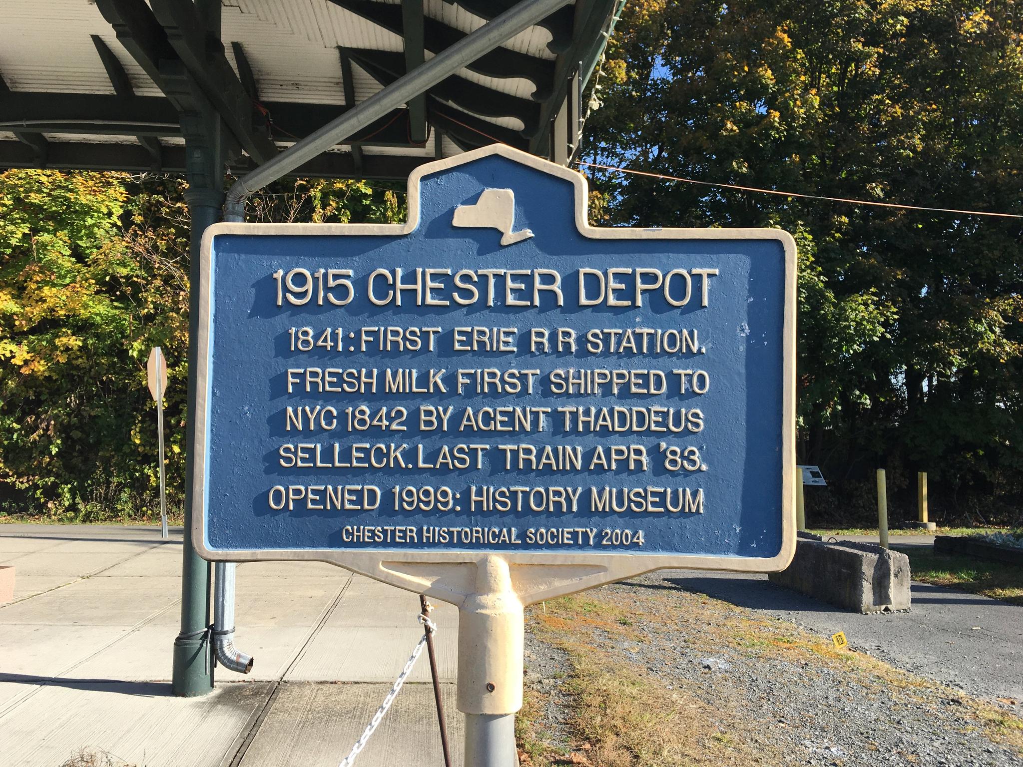 A blue historical marker under a shelter, detailing a 1915 depot.