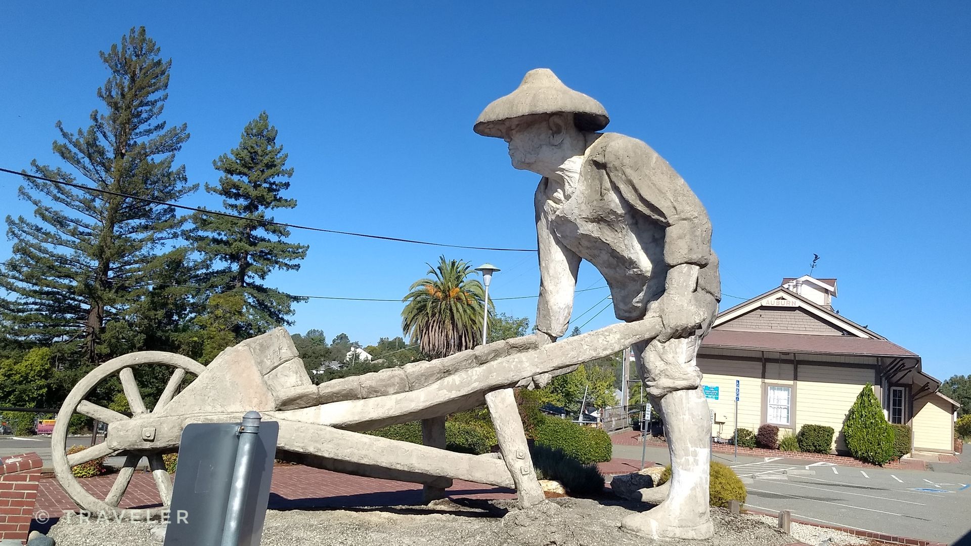 A stone statue of a person in a hat pushing a wheelbarrow. - Auburn Olive Orchard Loop