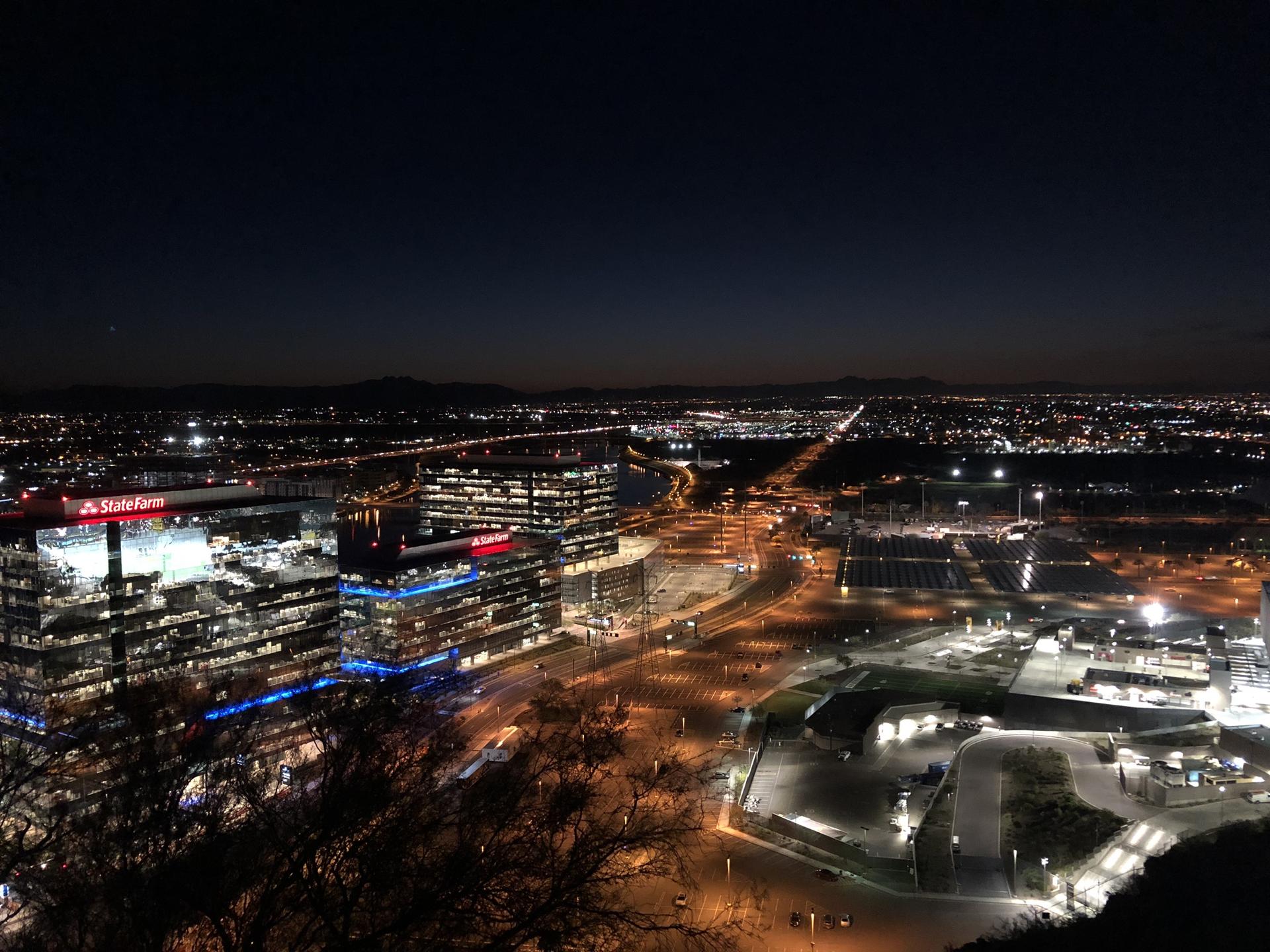 Nighttime cityscape from above, with brightly lit buildings and roads under a dark sky.