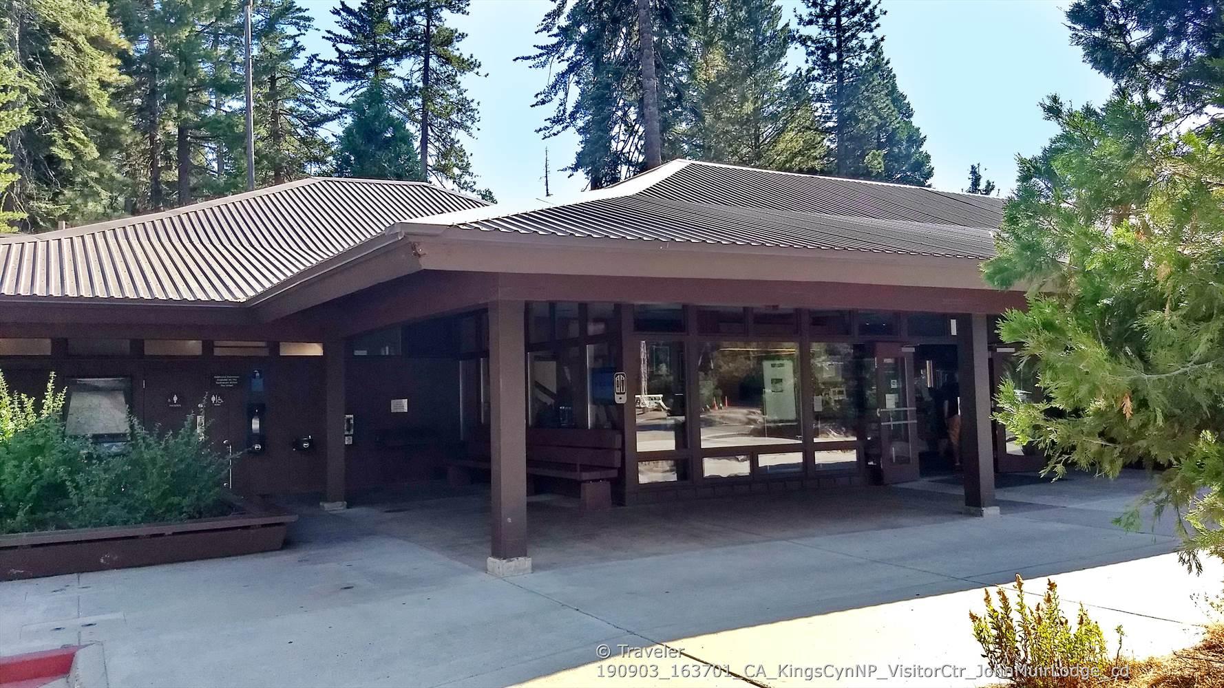Modern building with a brown roof and porch, surrounded by trees.