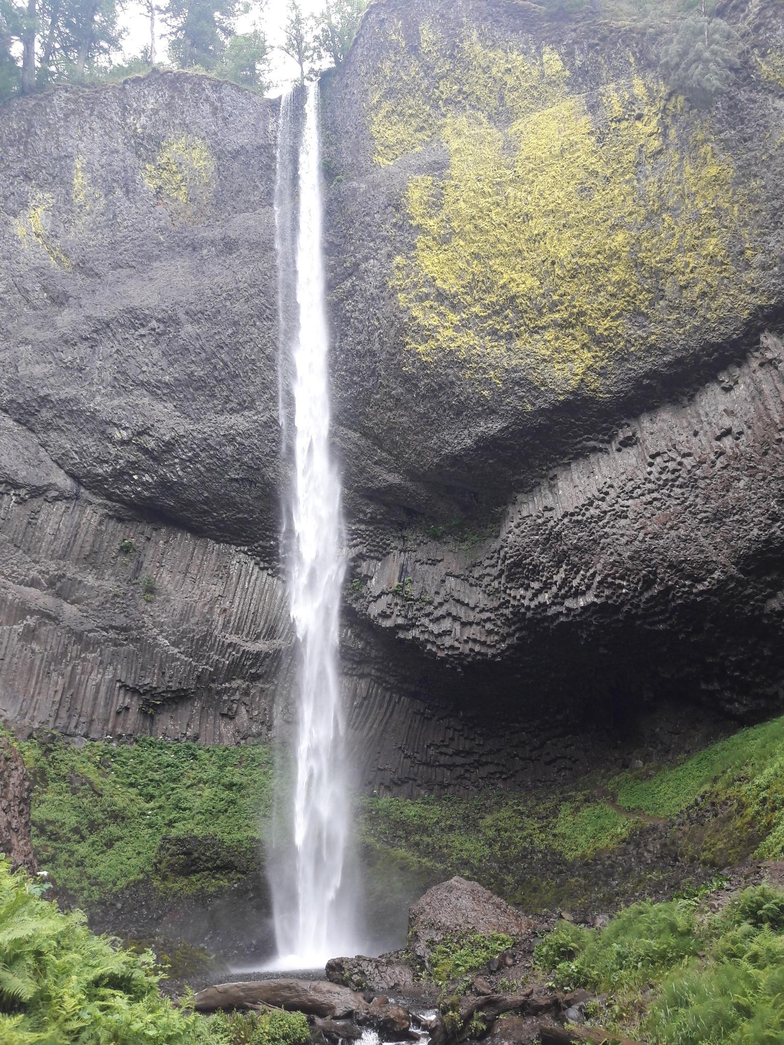 Tall, narrow waterfall plunges into a rocky basin with green moss.