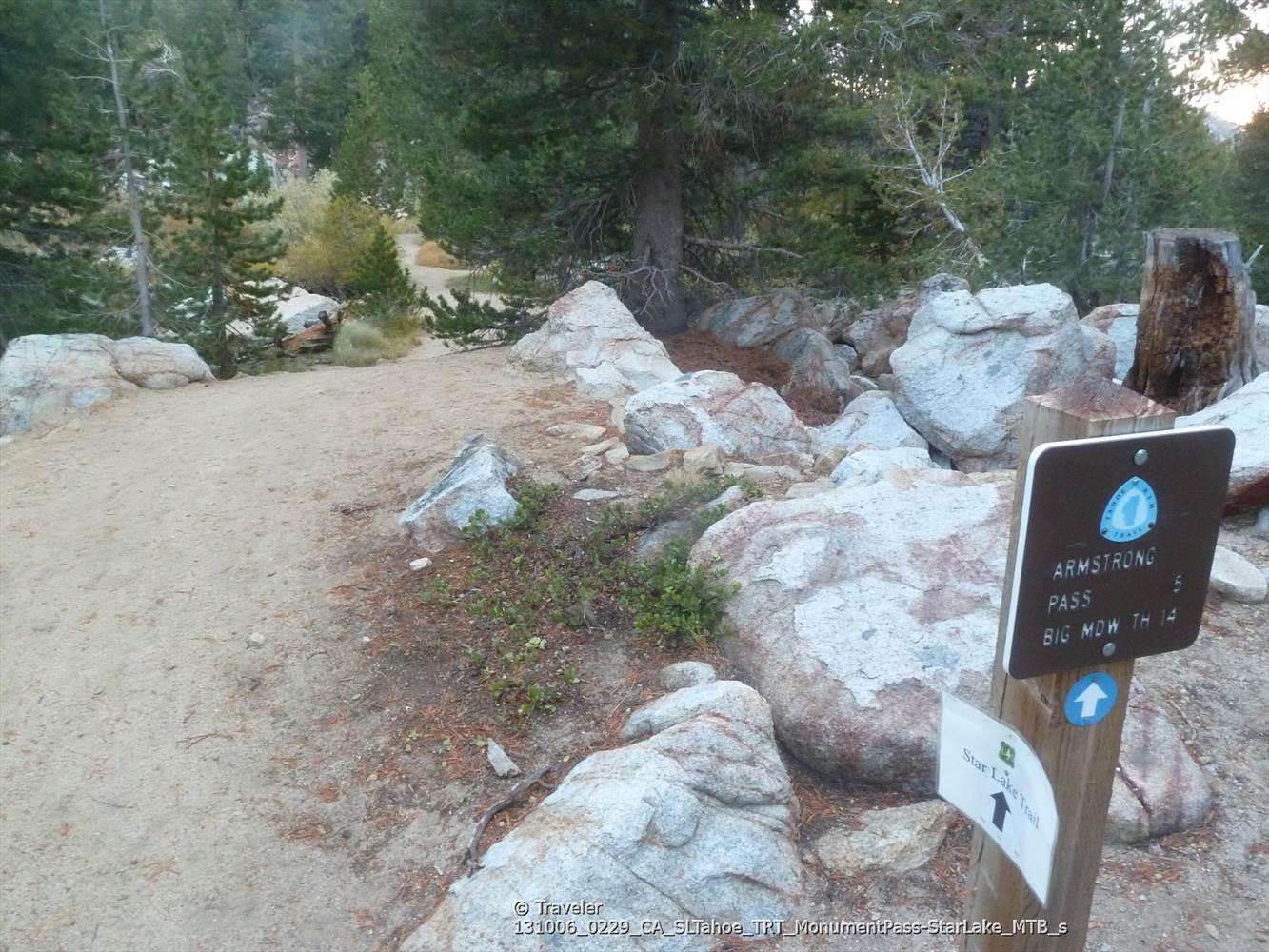 Dirt path leading into a forest, with large rocks and a wooden trail sign.