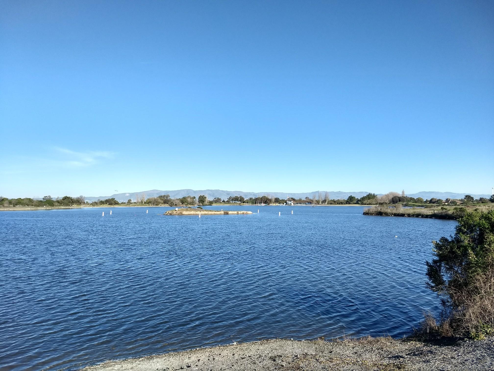 Expansive blue lake with distant mountains and clear sky.