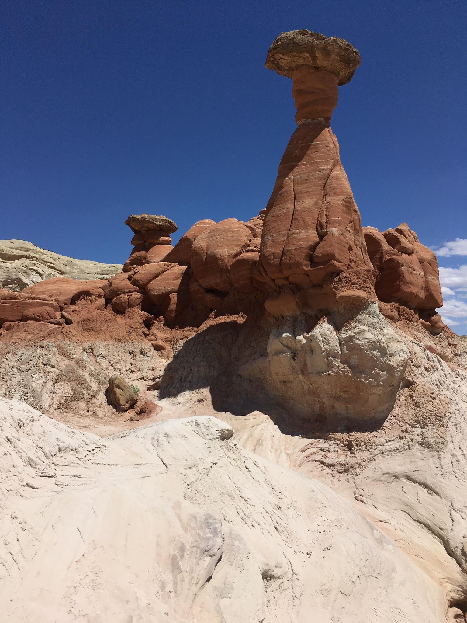 A tall, red and white hoodoo stands prominently against a clear blue sky.