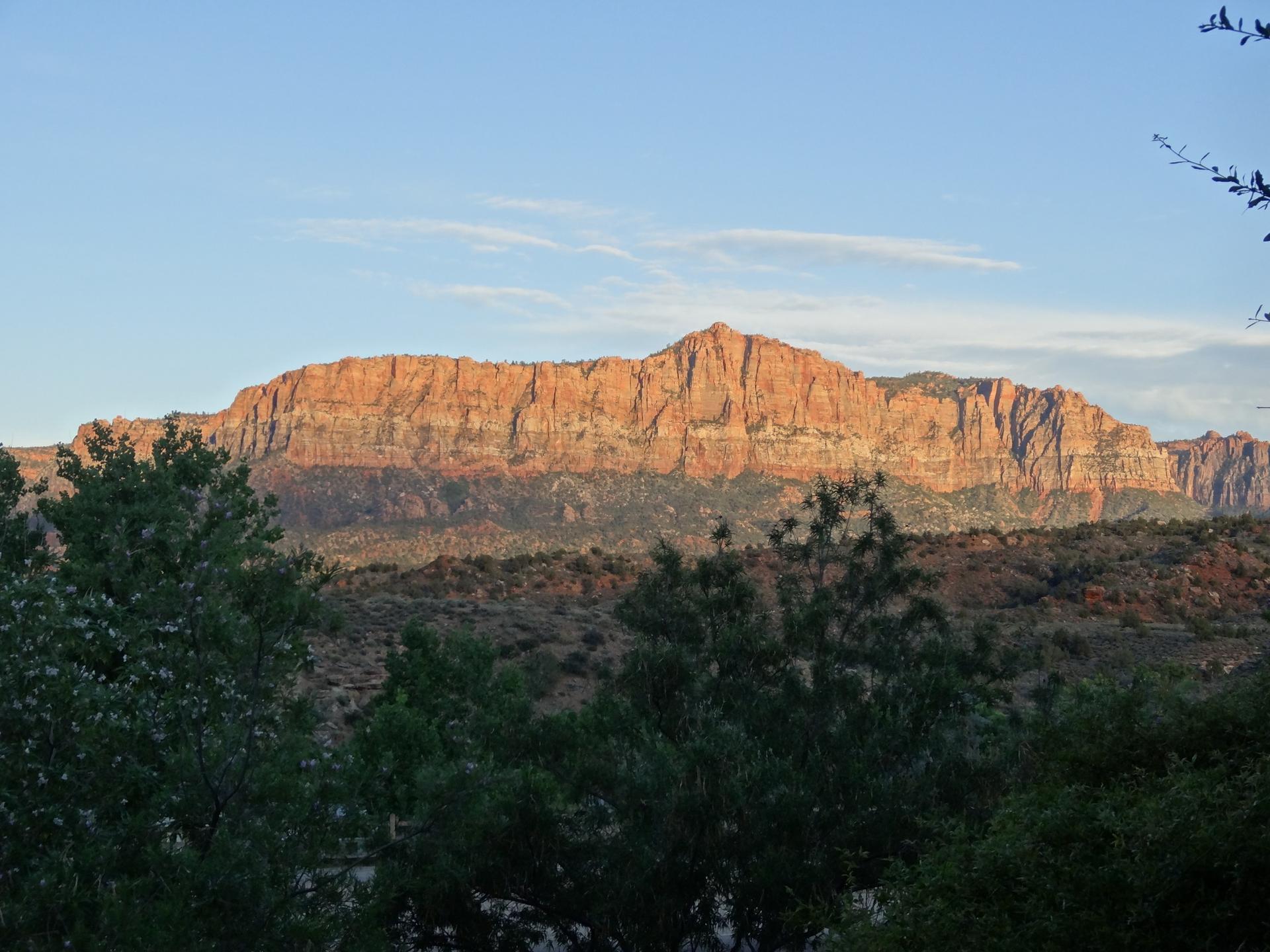 Wide view of a large, reddish mountain range under a clear sky.