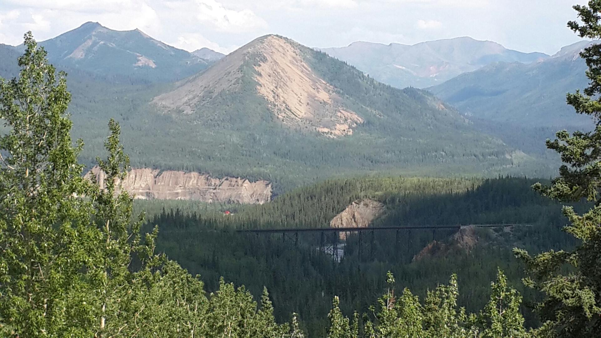 Panoramic view of forested mountains with a large bridge spanning a valley.