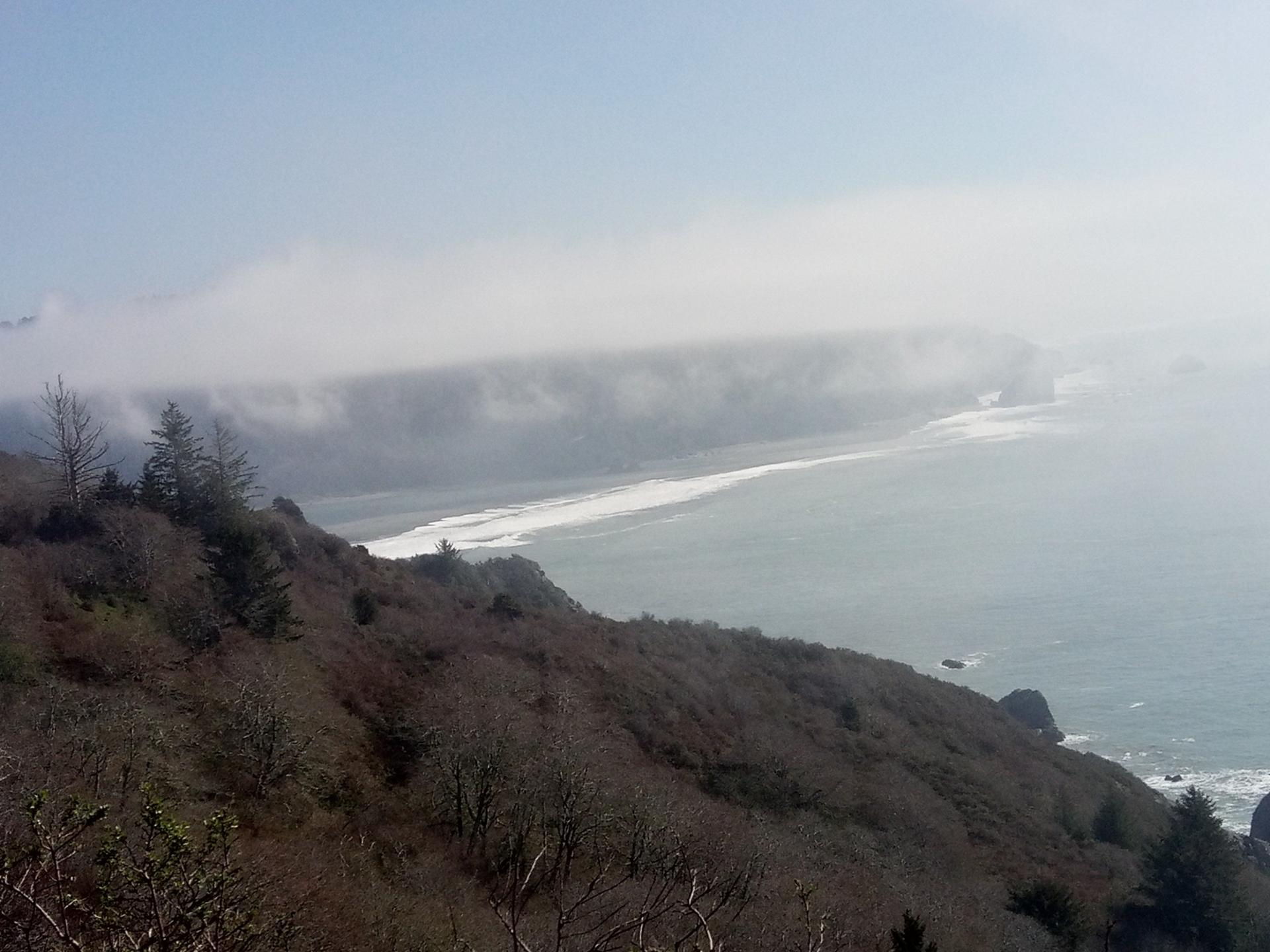 Foggy coastal view with a long beach and ocean waves from above.
