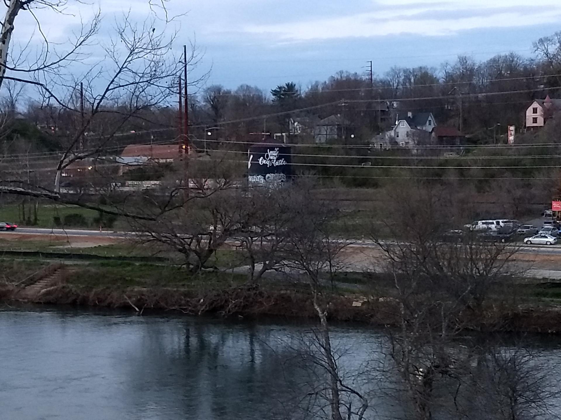 River in foreground with distant houses, bare trees, and road.
