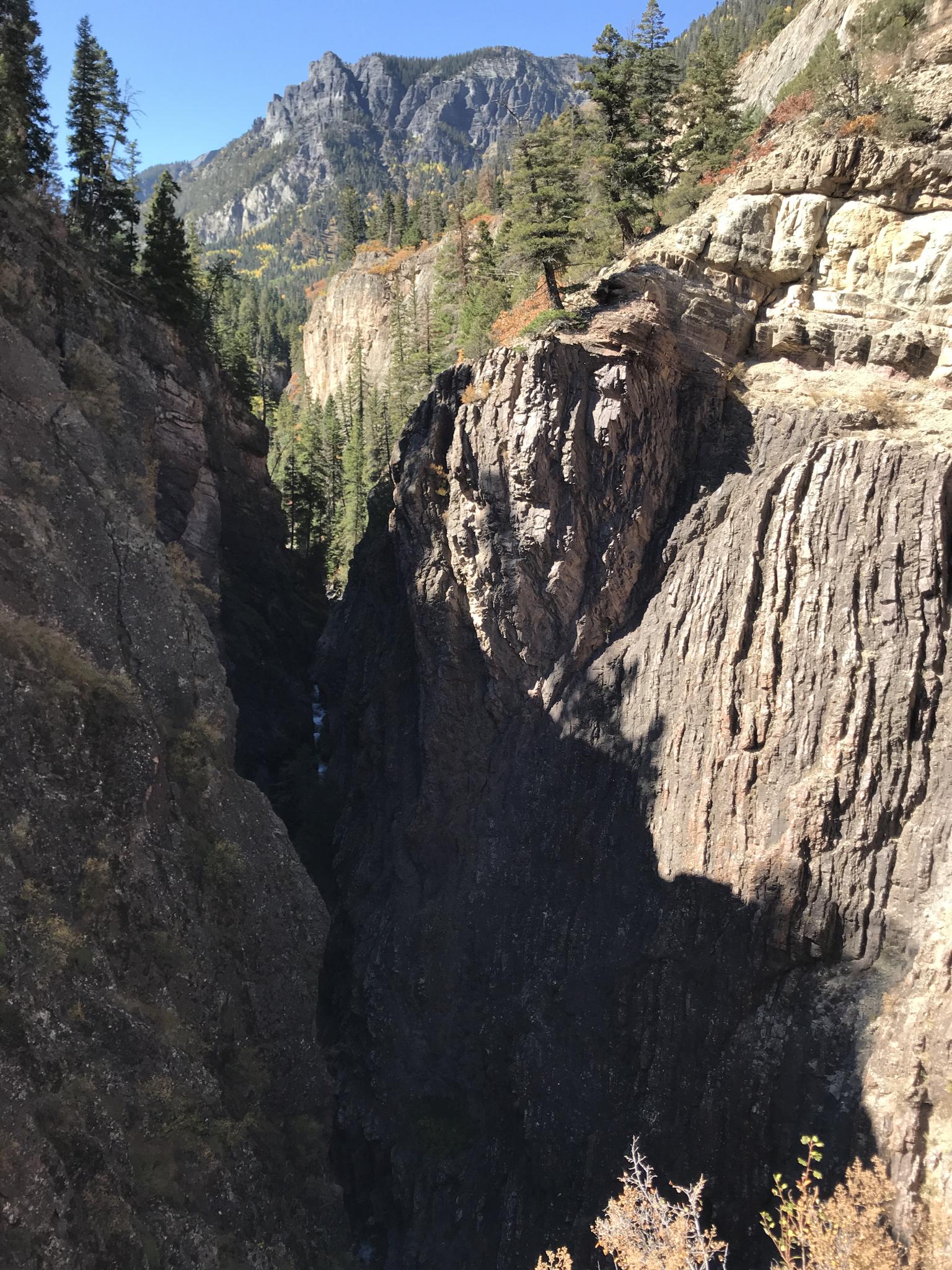 Deep, rocky canyon with a narrow gorge and distant mountains, bright sun.
