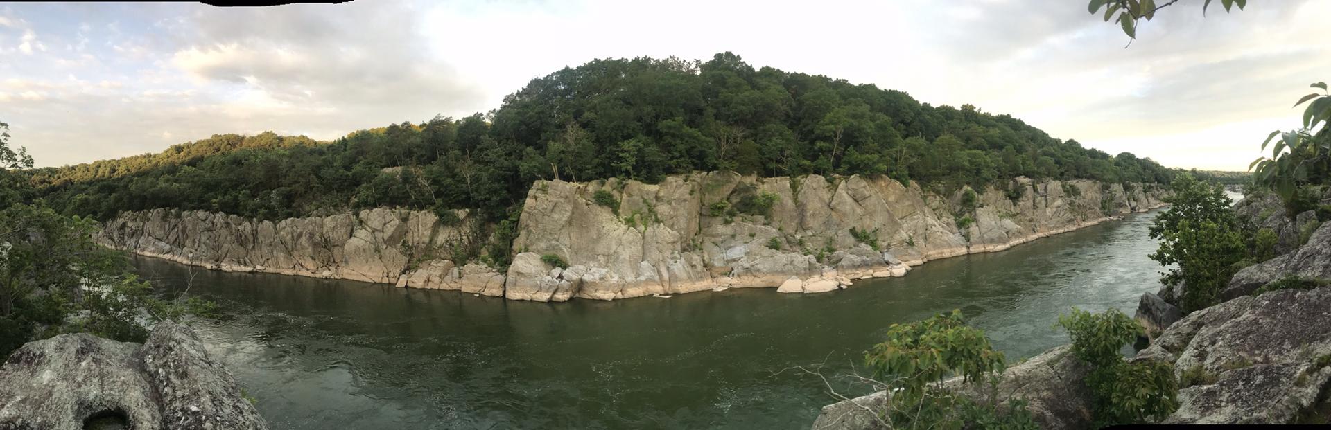 Wide river with rocky cliffs and dense green forest under an overcast sky.