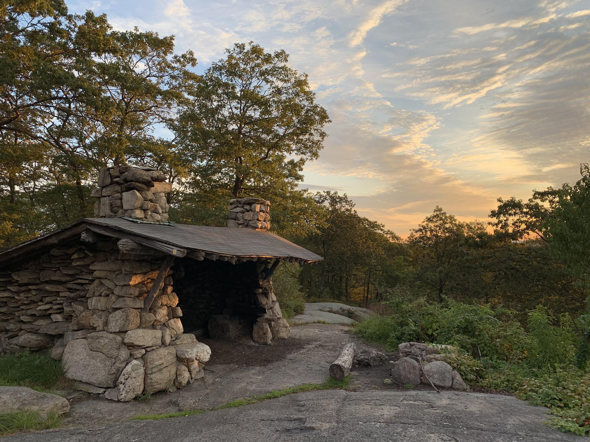 A rustic stone shelter at sunset, surrounded by trees and warm light.