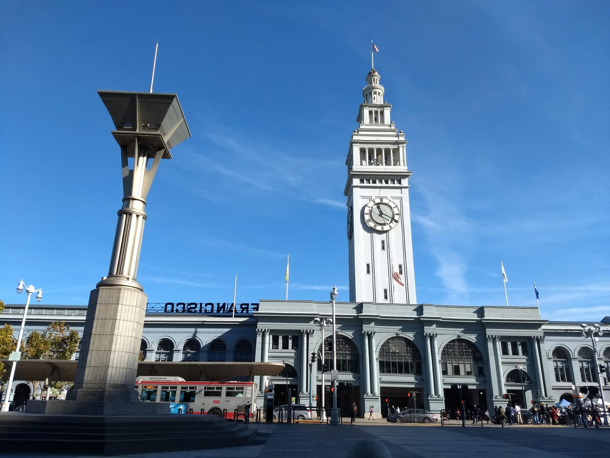 Tall clock tower building and modern sculpture under clear blue sky.