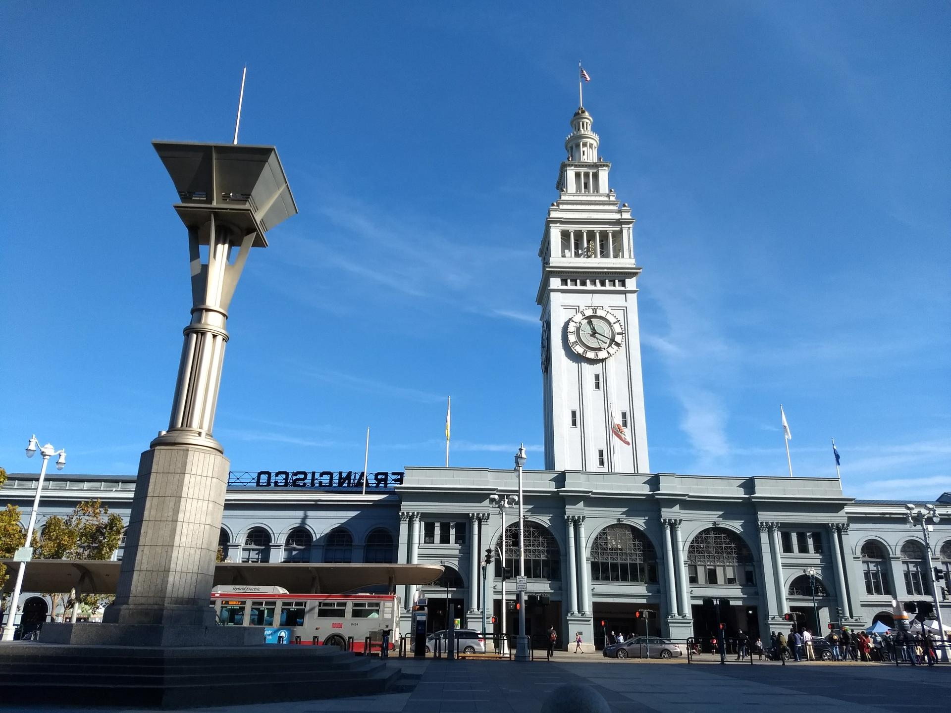 Tall clock tower building and modern sculpture under clear blue sky.
