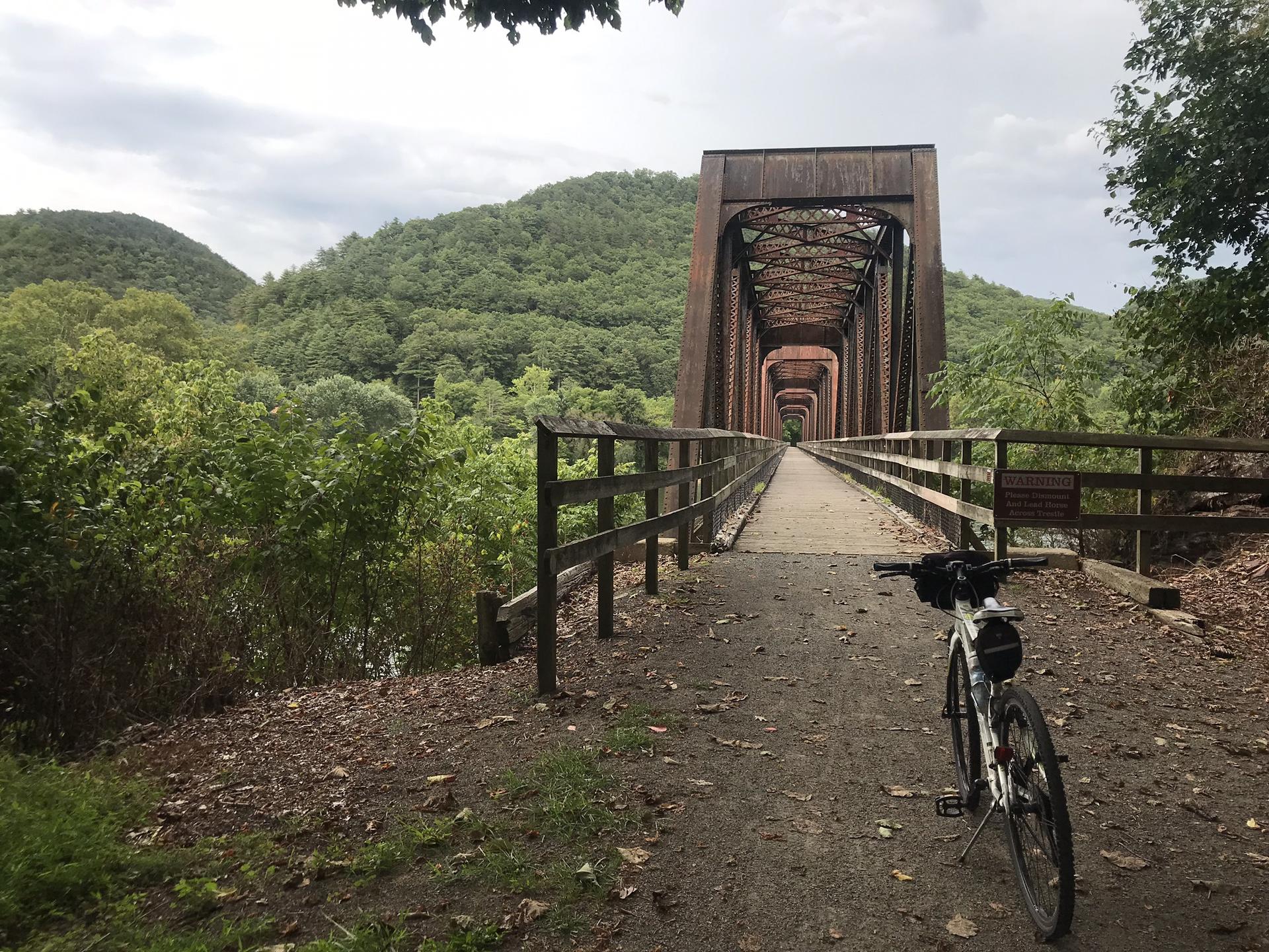 Bicycle parked on a dirt path leading to a large metal bridge.