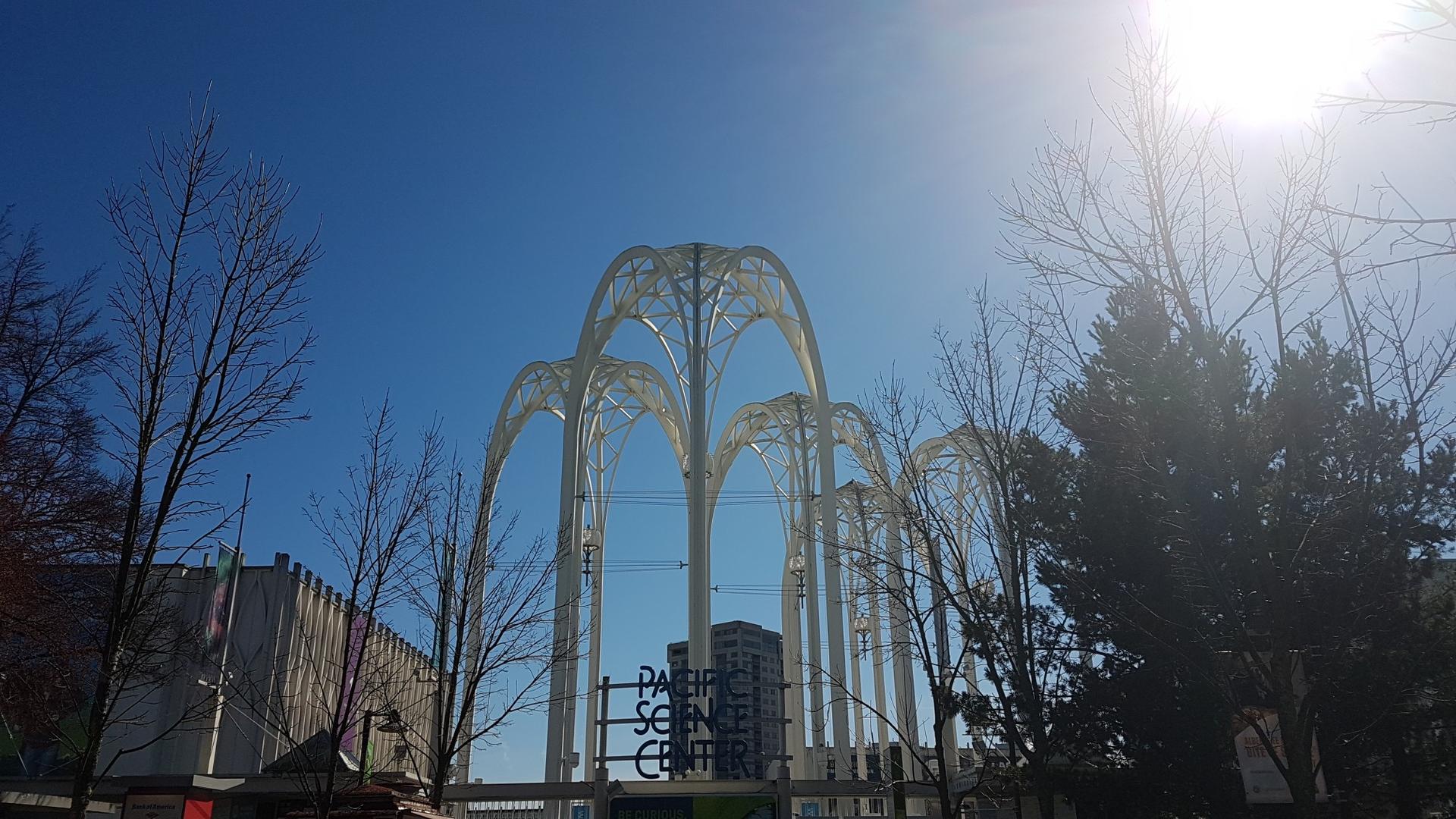 Modern architectural arches against a bright blue sky with sun glare.