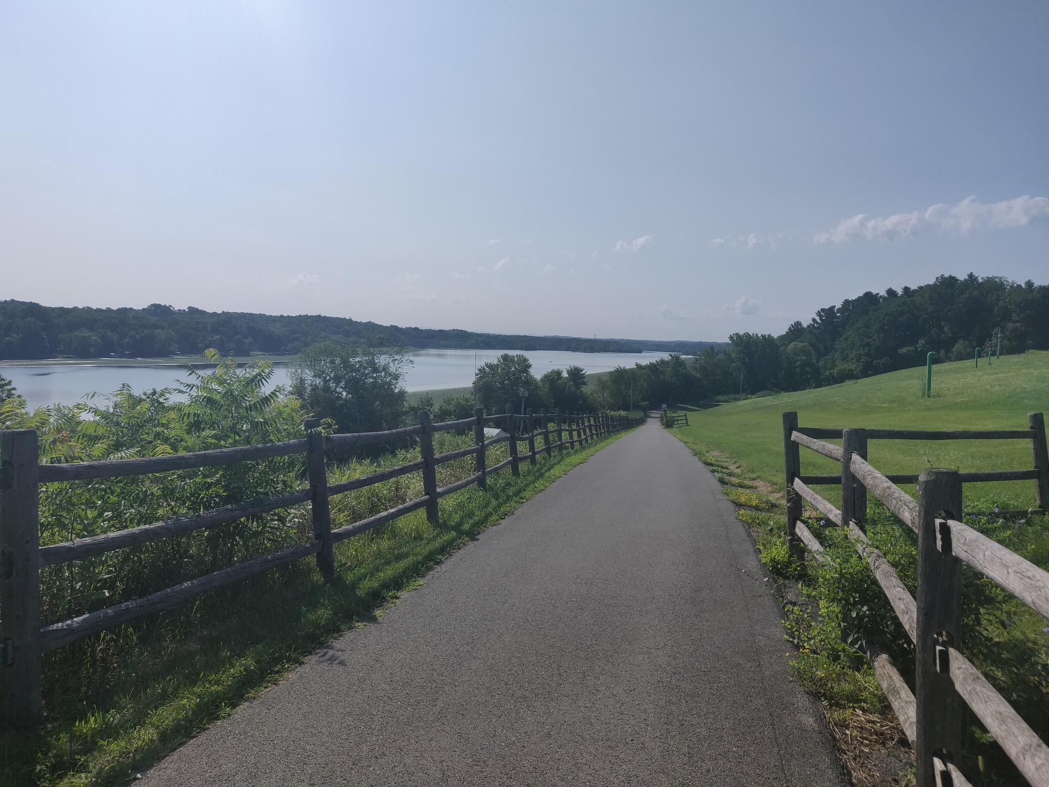 Paved path alongside a large body of water, sunny day.