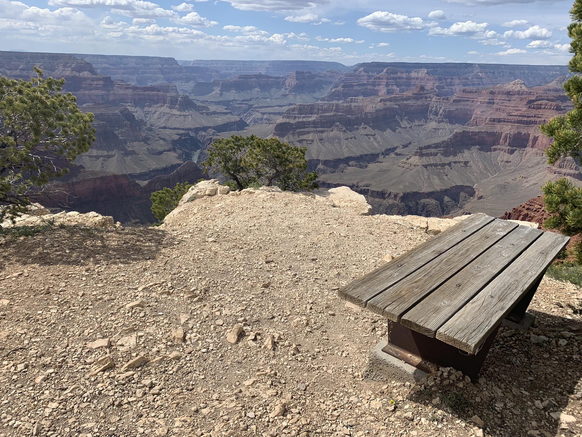 Wooden bench on a rocky overlook, facing a vast, layered canyon.