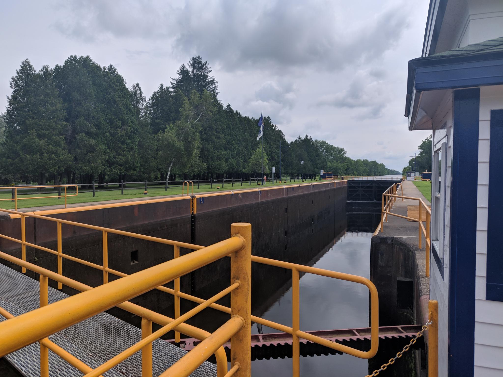A canal lock with dark water, yellow railings, and a cloudy sky.