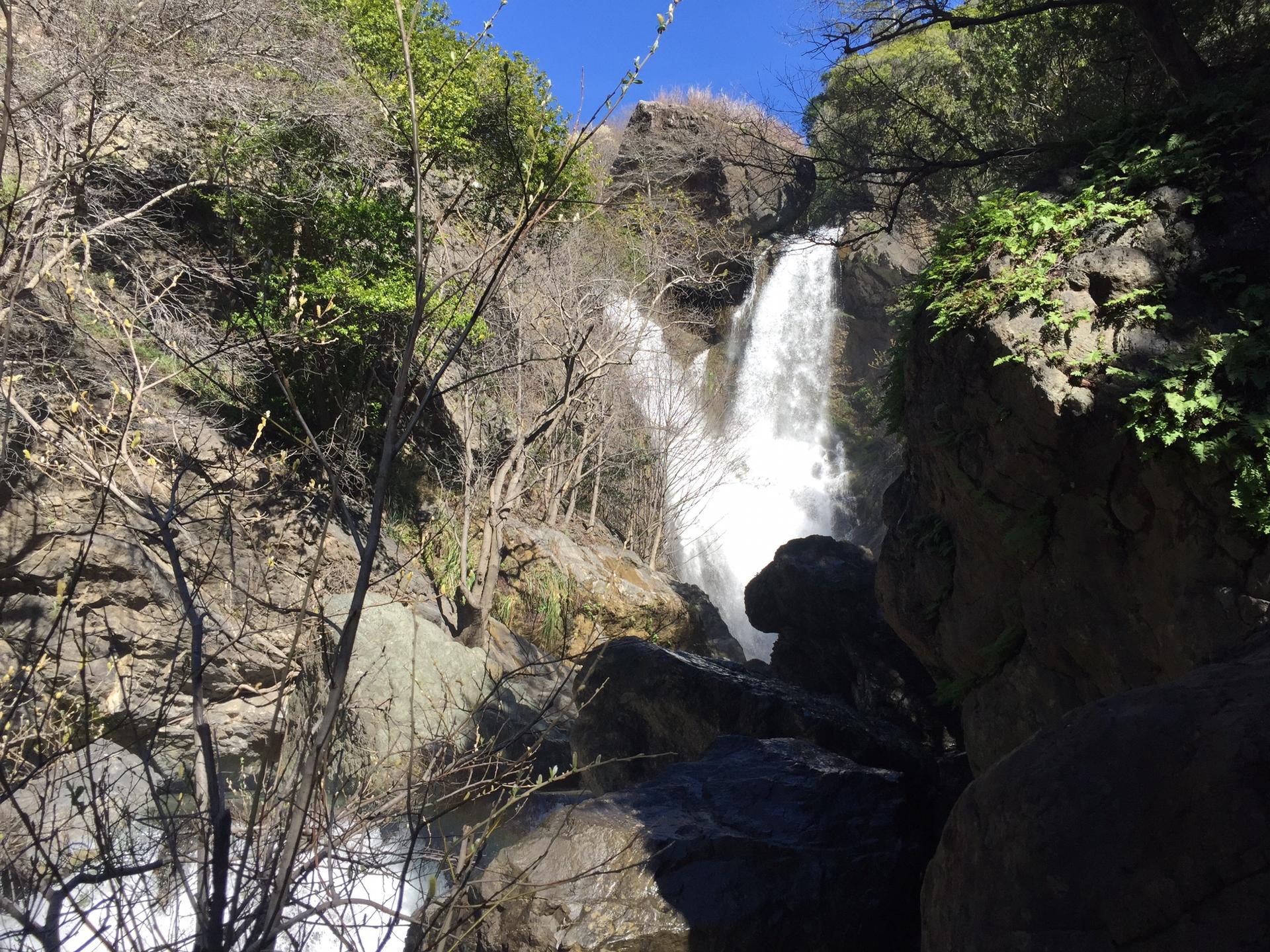 Powerful waterfall cascading down a rocky cliff surrounded by green trees.