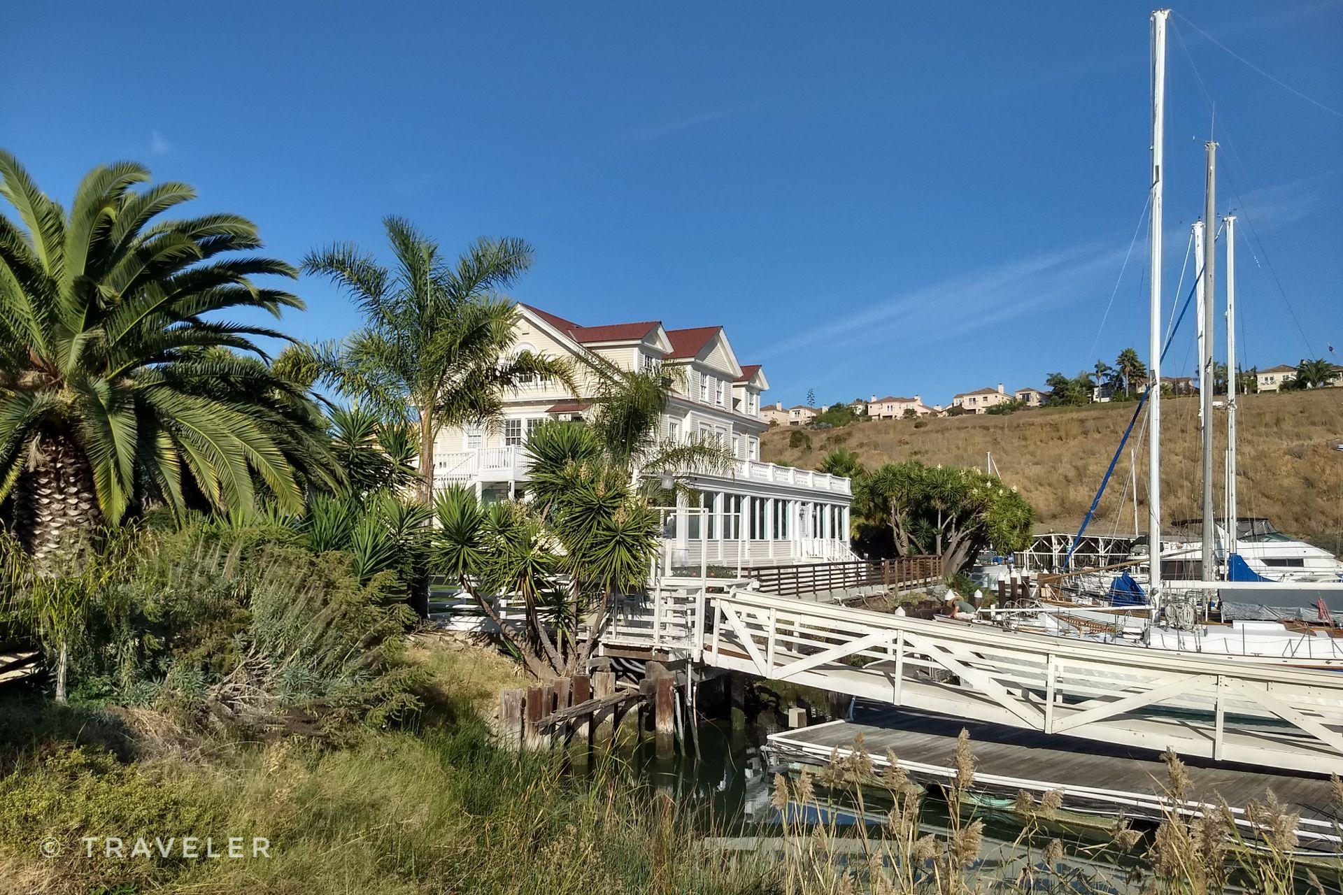 A large white building overlooks a marina with boats on a sunny day.