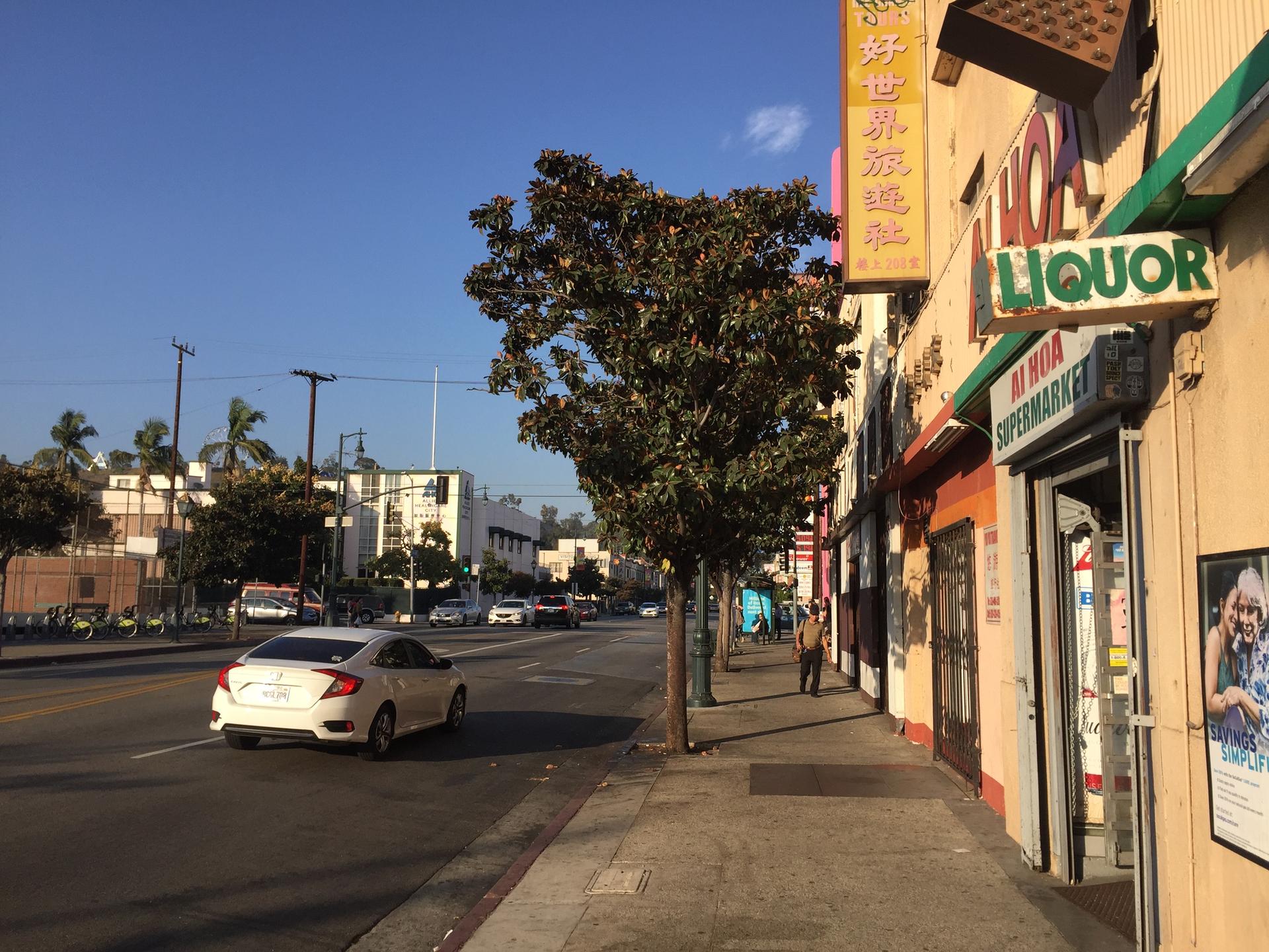 Sunny urban street with a white car, storefronts, and a person walking.