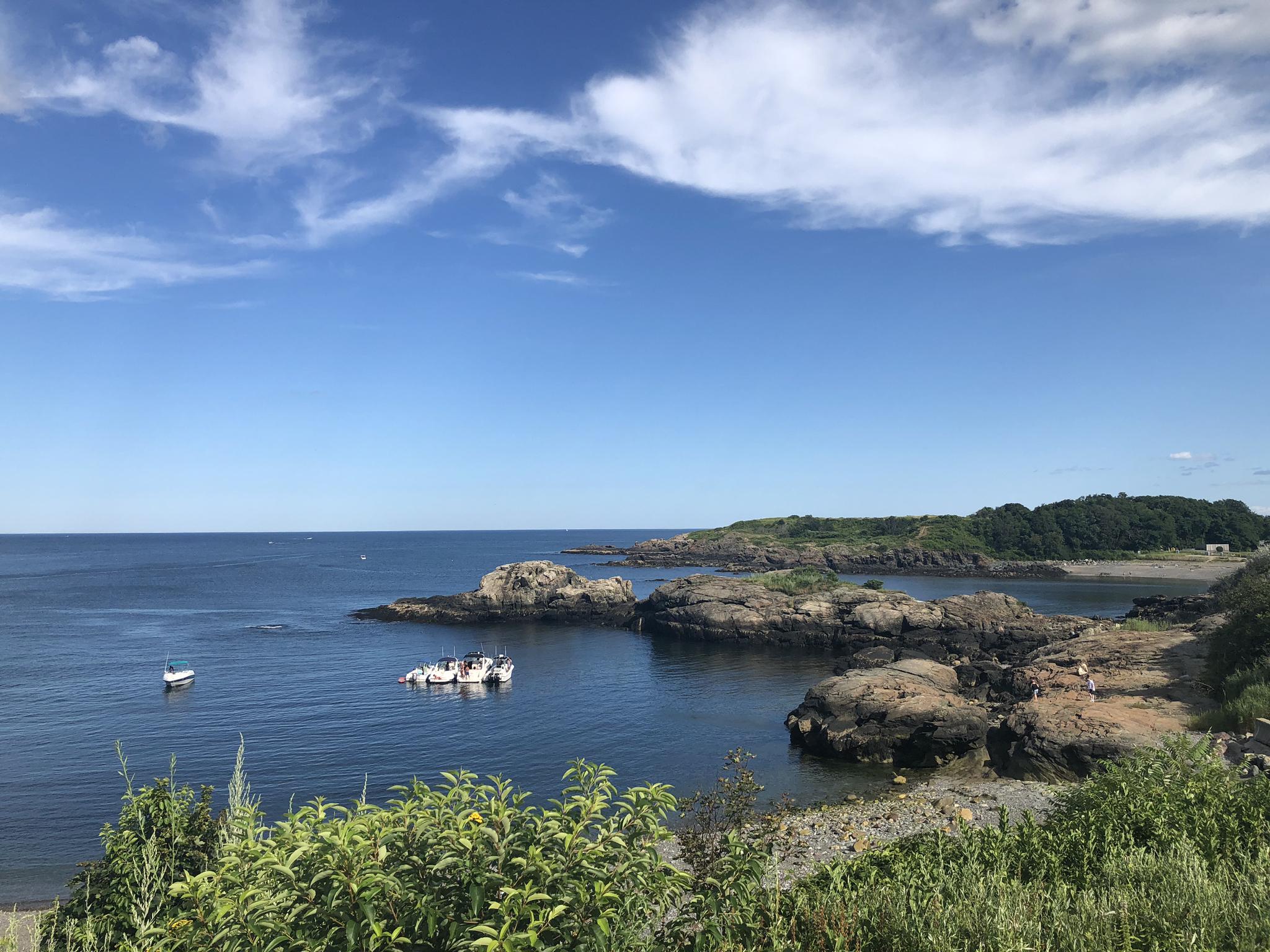Rocky coastline with boats in a calm cove under a bright blue sky.