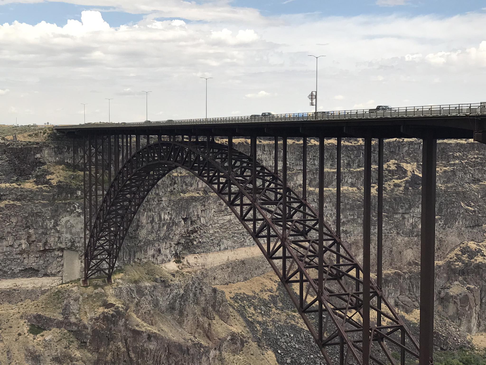 A massive steel arch bridge spans a deep, rocky canyon on a cloudy day.