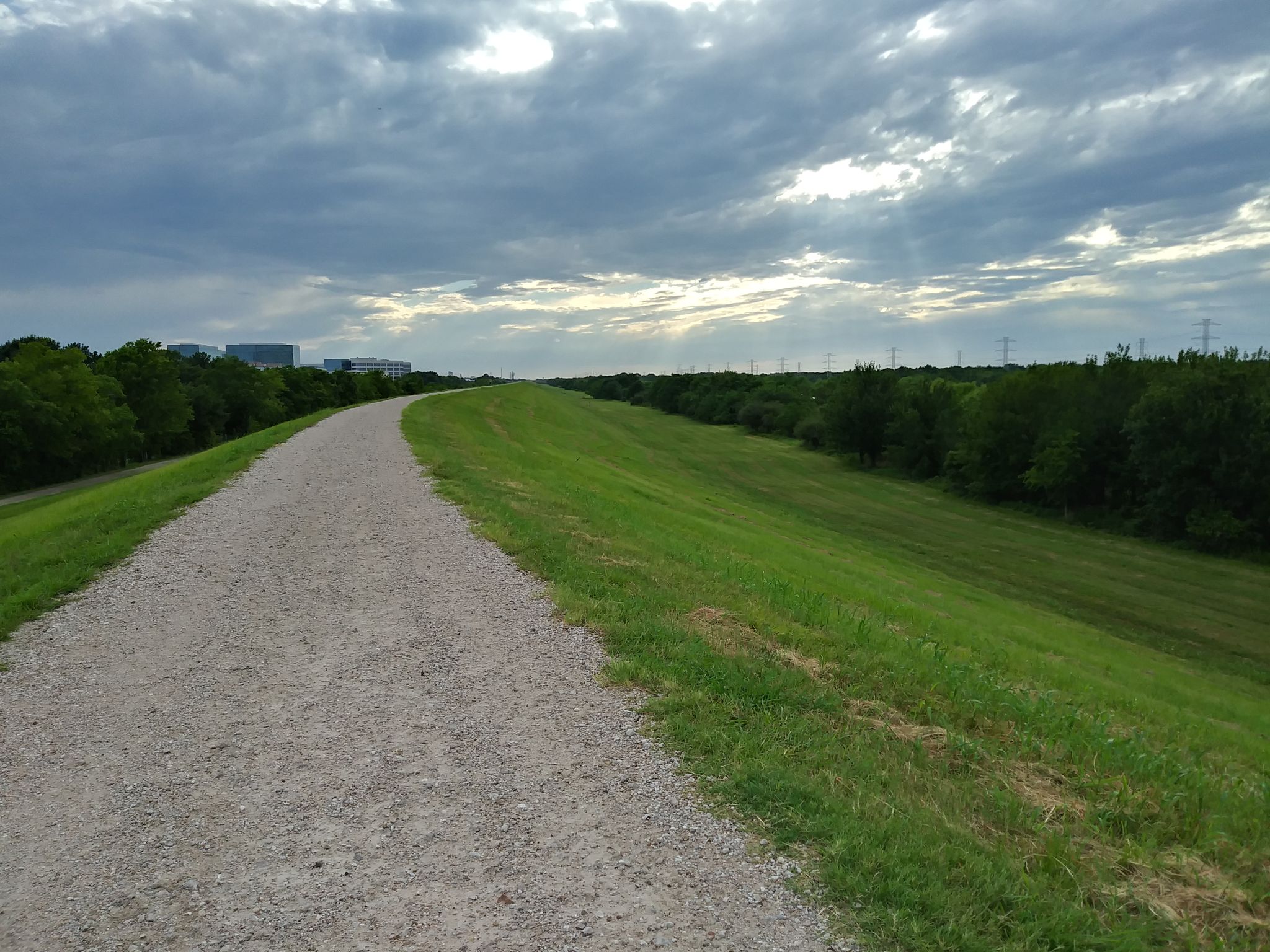 Gravel path on a grassy embankment under a cloudy sky with distant trees. - Buffalo Bayou loop from Downtown Houston
