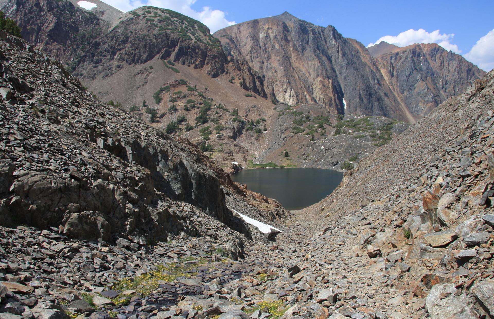 High-altitude rocky mountain landscape with a dark lake and patches of snow.