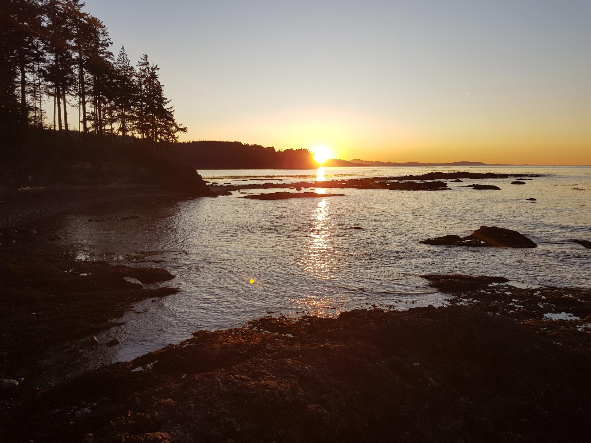 Bright sunset over a rocky coastline with sun reflecting on water.
