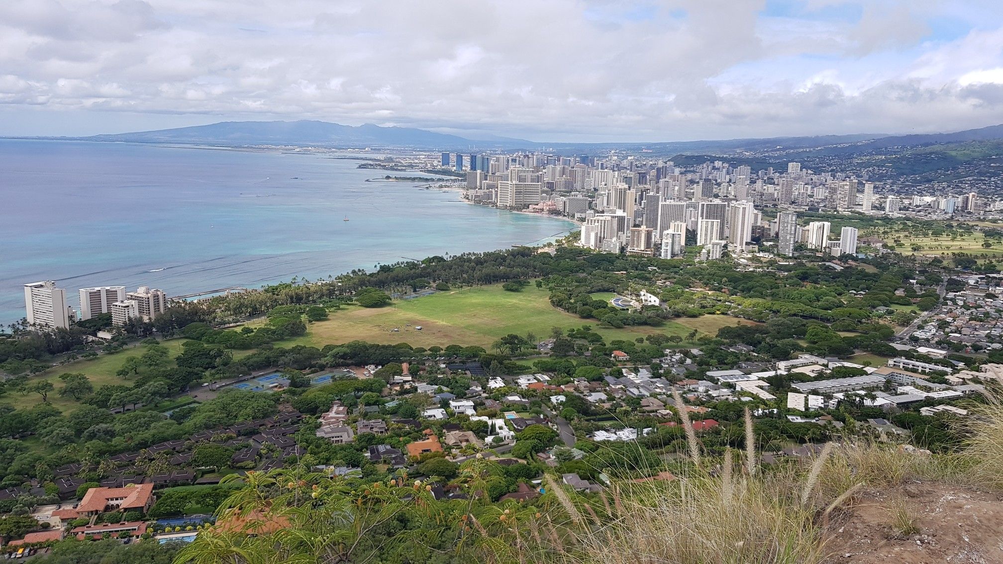 Overcast view of a coastal city, green park, and distant mountains. - Diamond Head loop from Waikiki