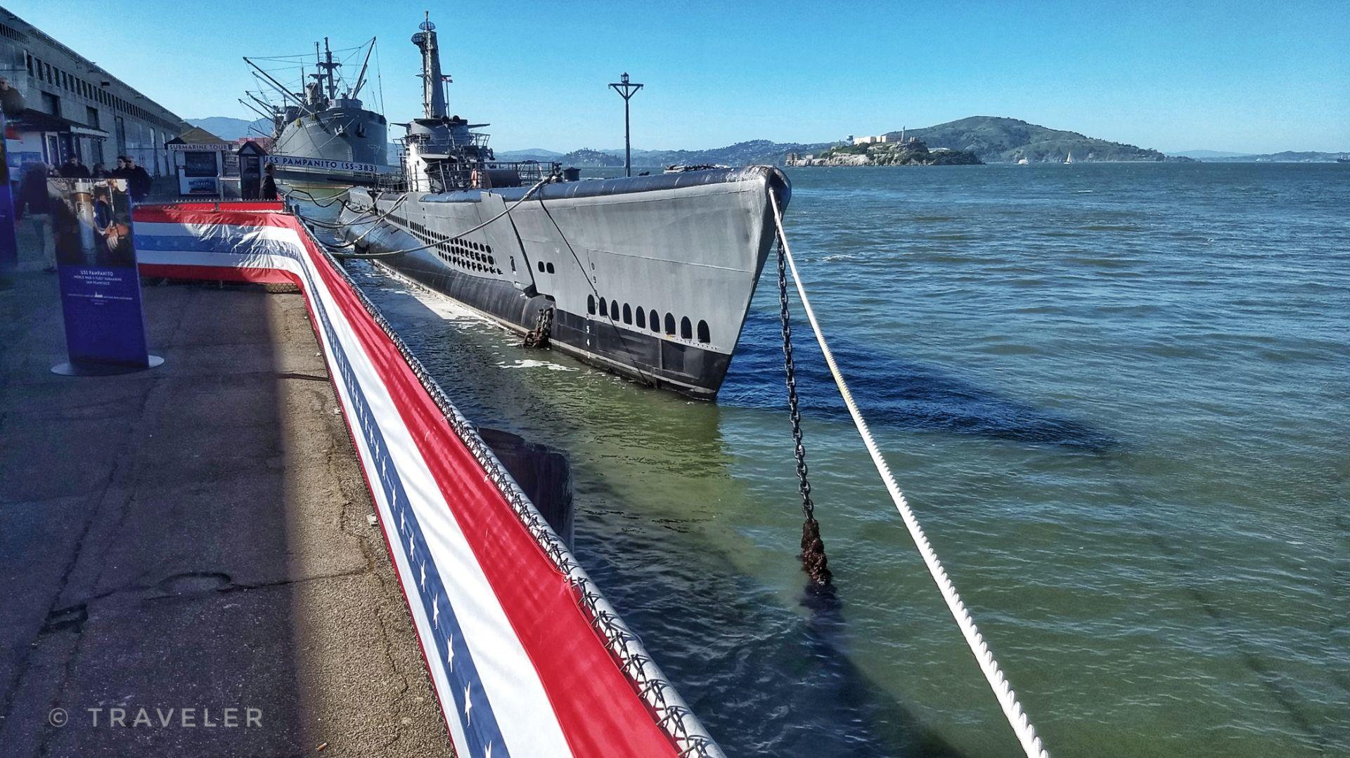 Submarine docked at a pier with red, white, and blue bunting.