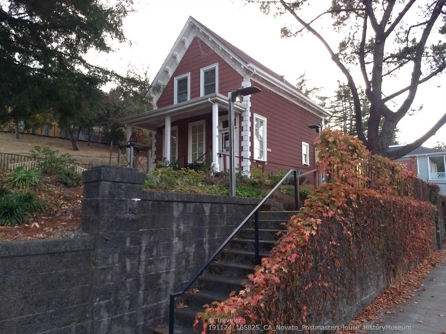 Red house on a hill, with stone wall, stairs, and autumn vines.