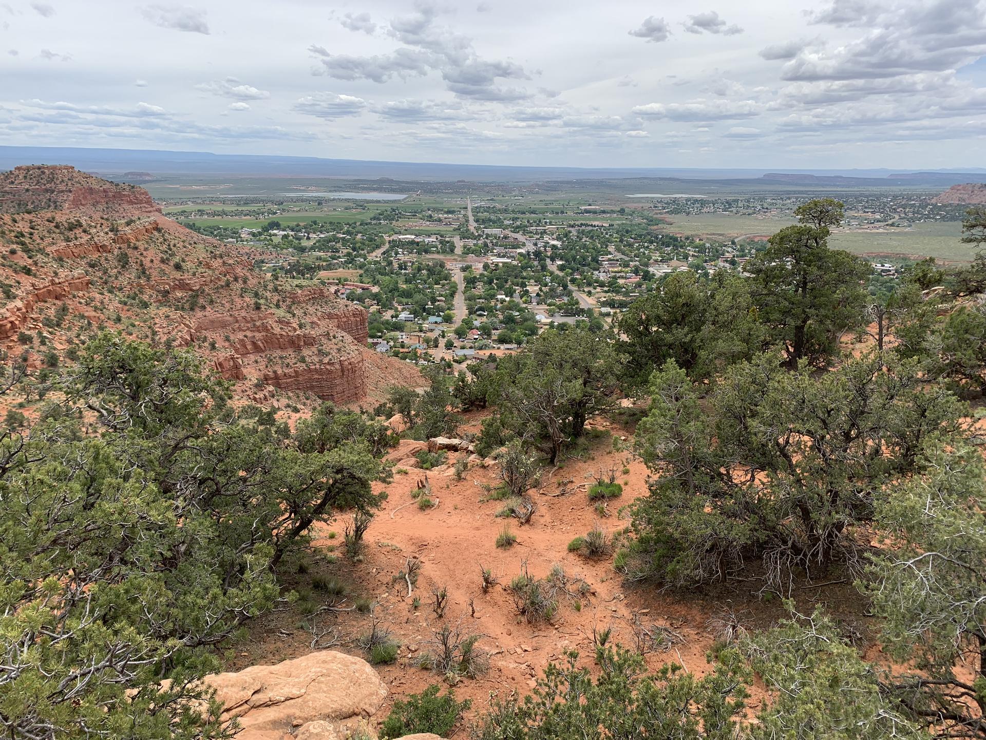 Overlook of a green valley town from a rocky, tree-covered hill.