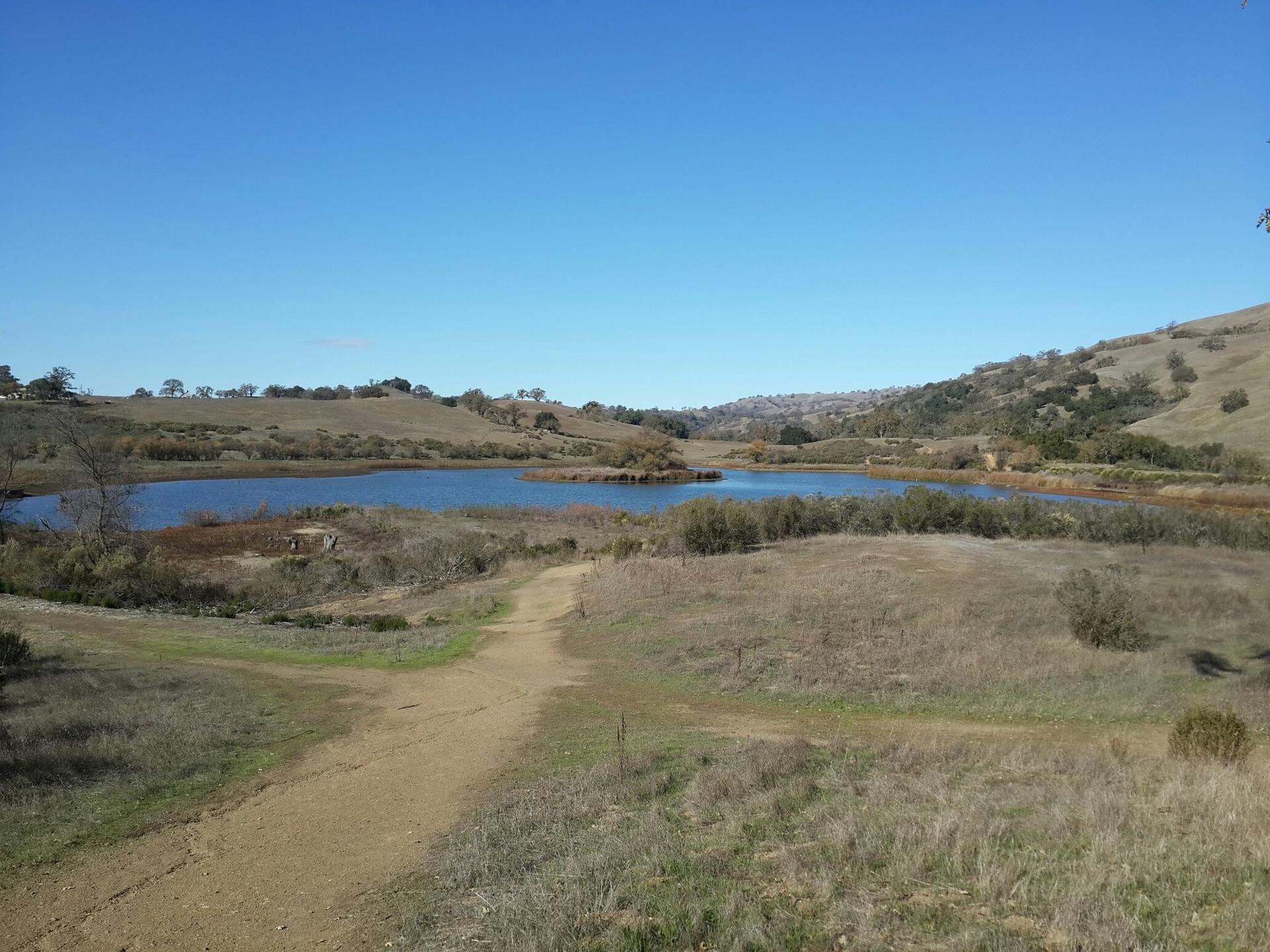 A dirt path leads to a calm lake surrounded by dry hills.