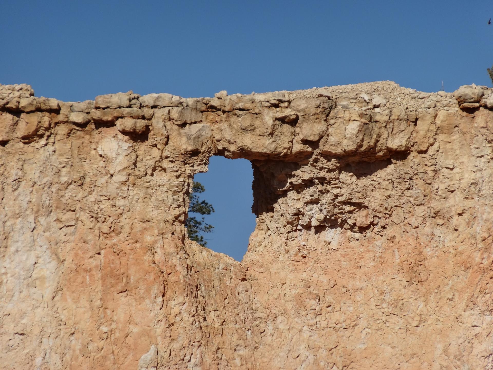A natural window in a reddish rock wall under a clear blue sky.