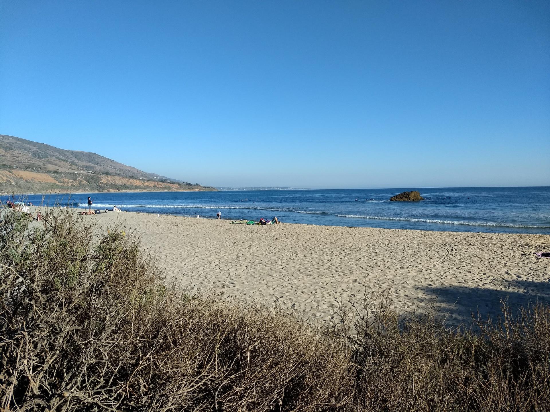 A wide sandy beach meets calm blue ocean under a clear sky.