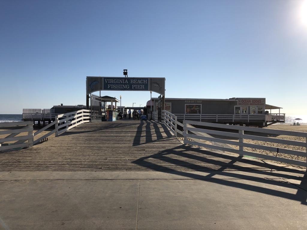 Pier entrance with buildings under a bright sunny sky, casting long shadows.