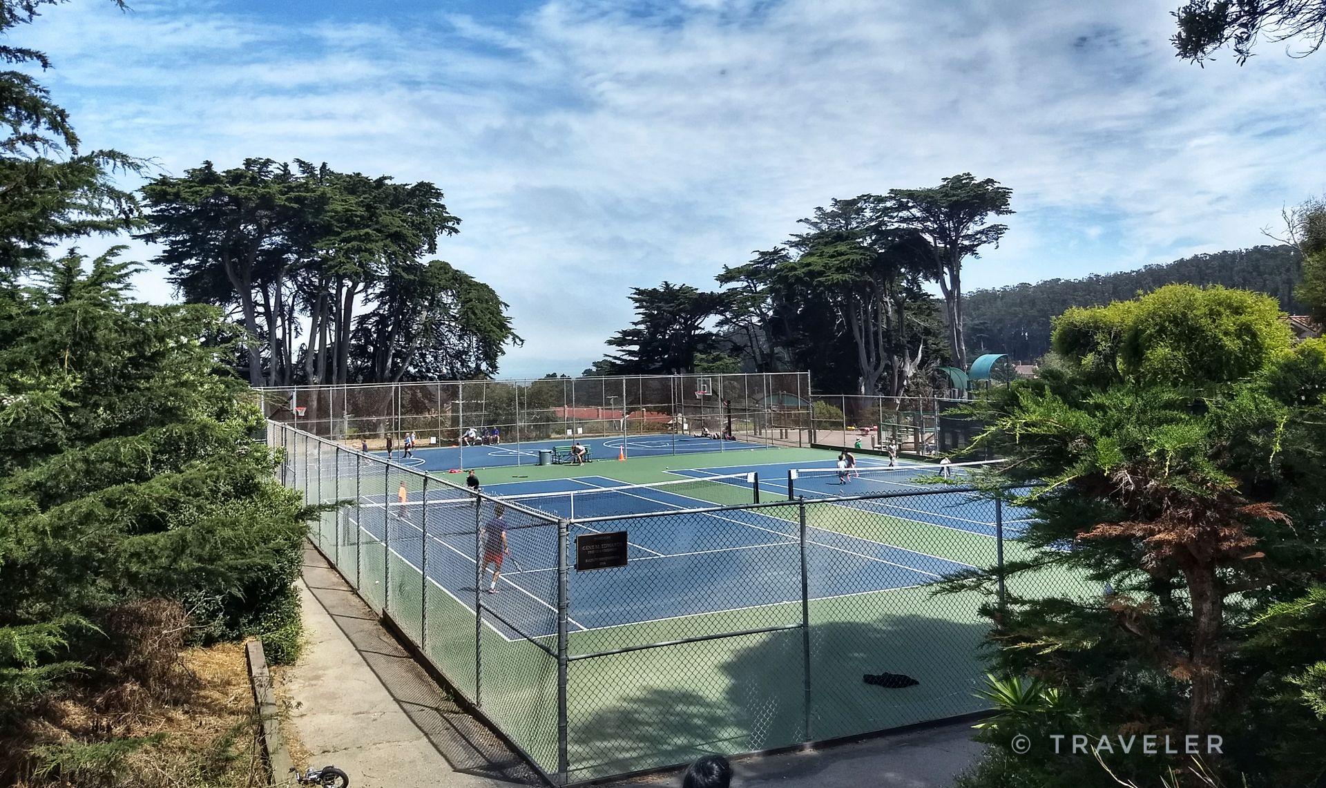 Aerial view of multiple blue and green tennis courts with players.