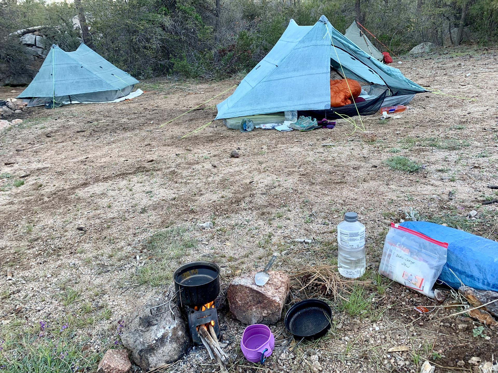 A campsite with two light blue tents and a cooking pot over a small fire.