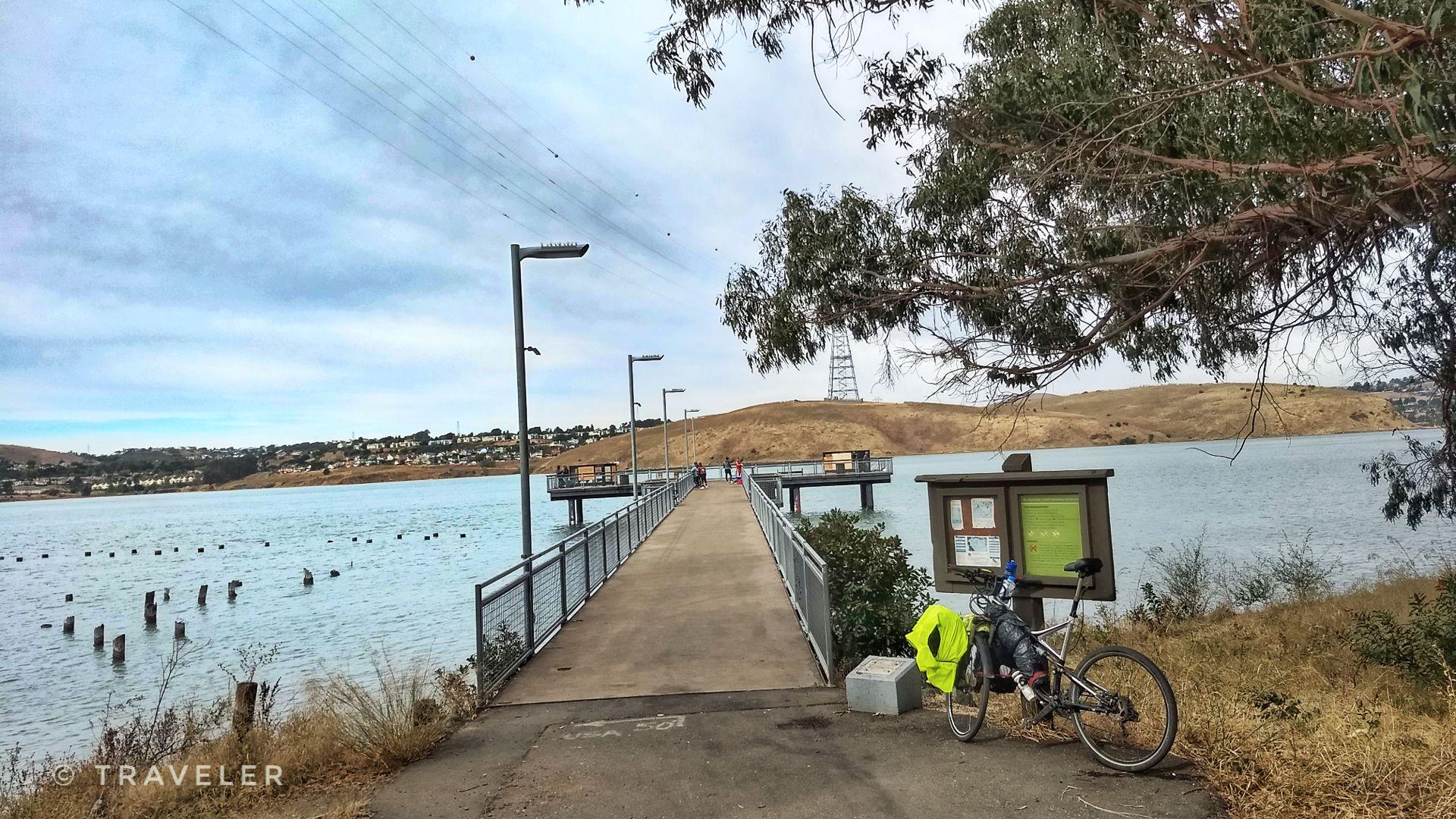 Bicycle parked beside a concrete pier extending into a large body of water.
