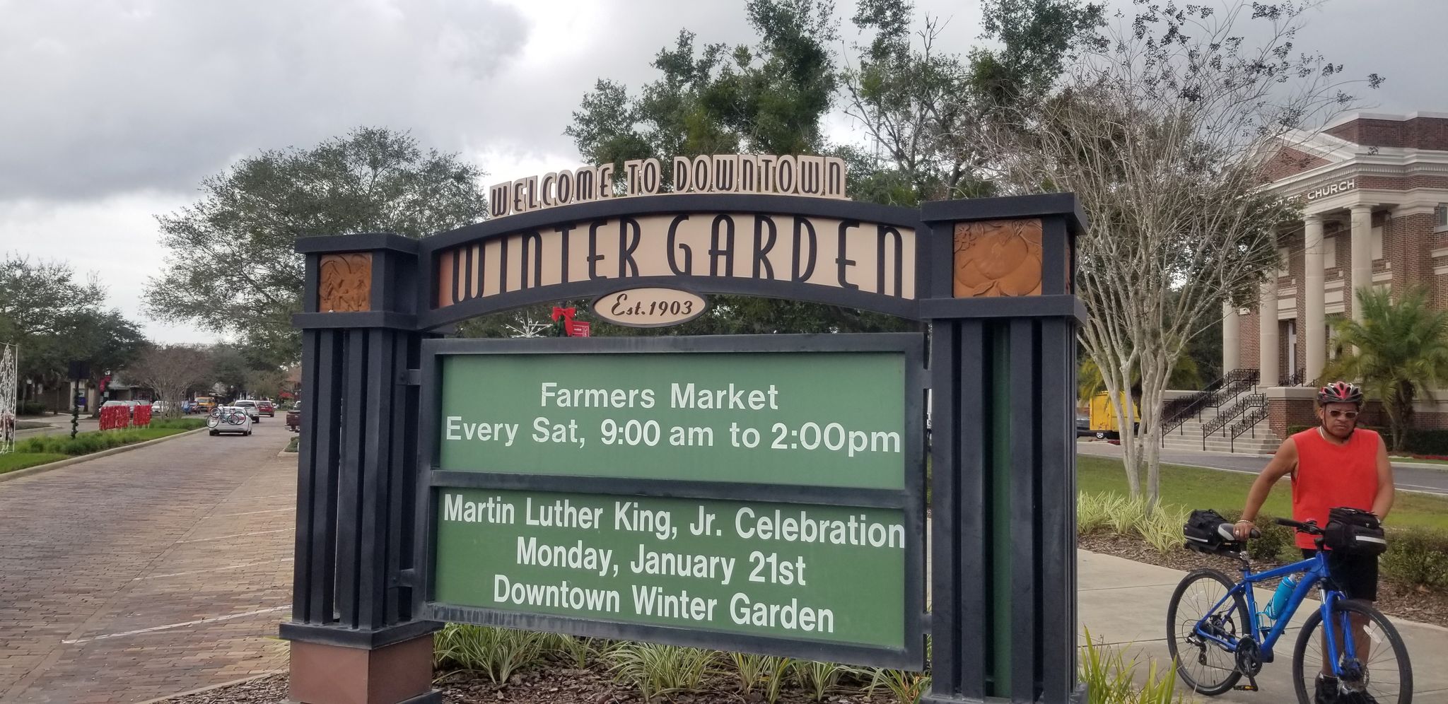 Overcast day with a large sign and a person standing with a bicycle. - West Orange Trail – Downtown Winter Garden loop from Winter Garden