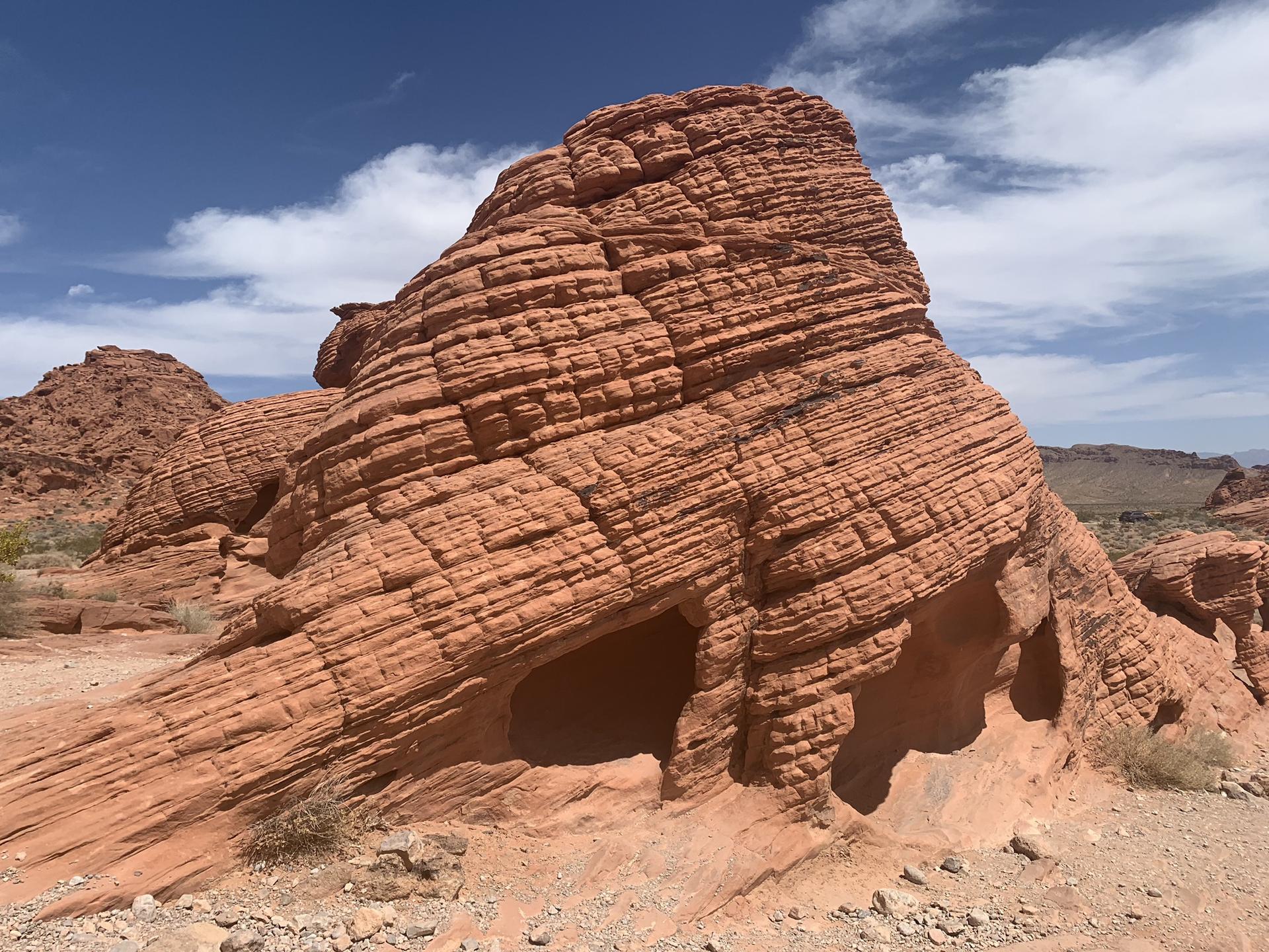 Large layered red rock formation with a small cave, under a blue sky.
