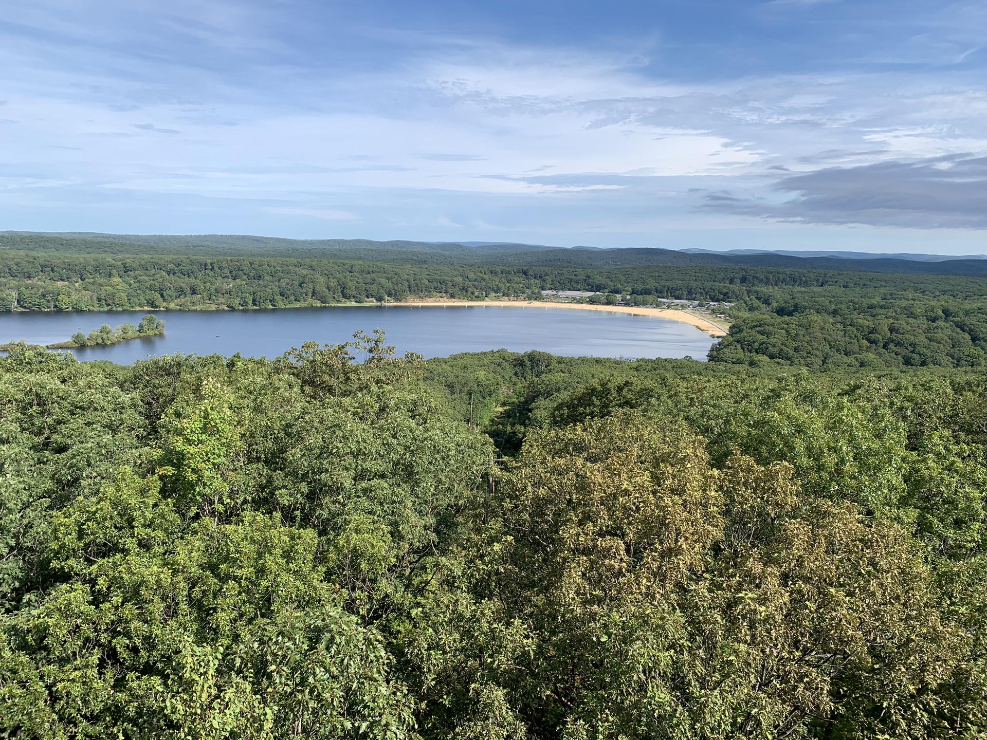 Aerial view of a large lake with a sandy beach surrounded by green forest.