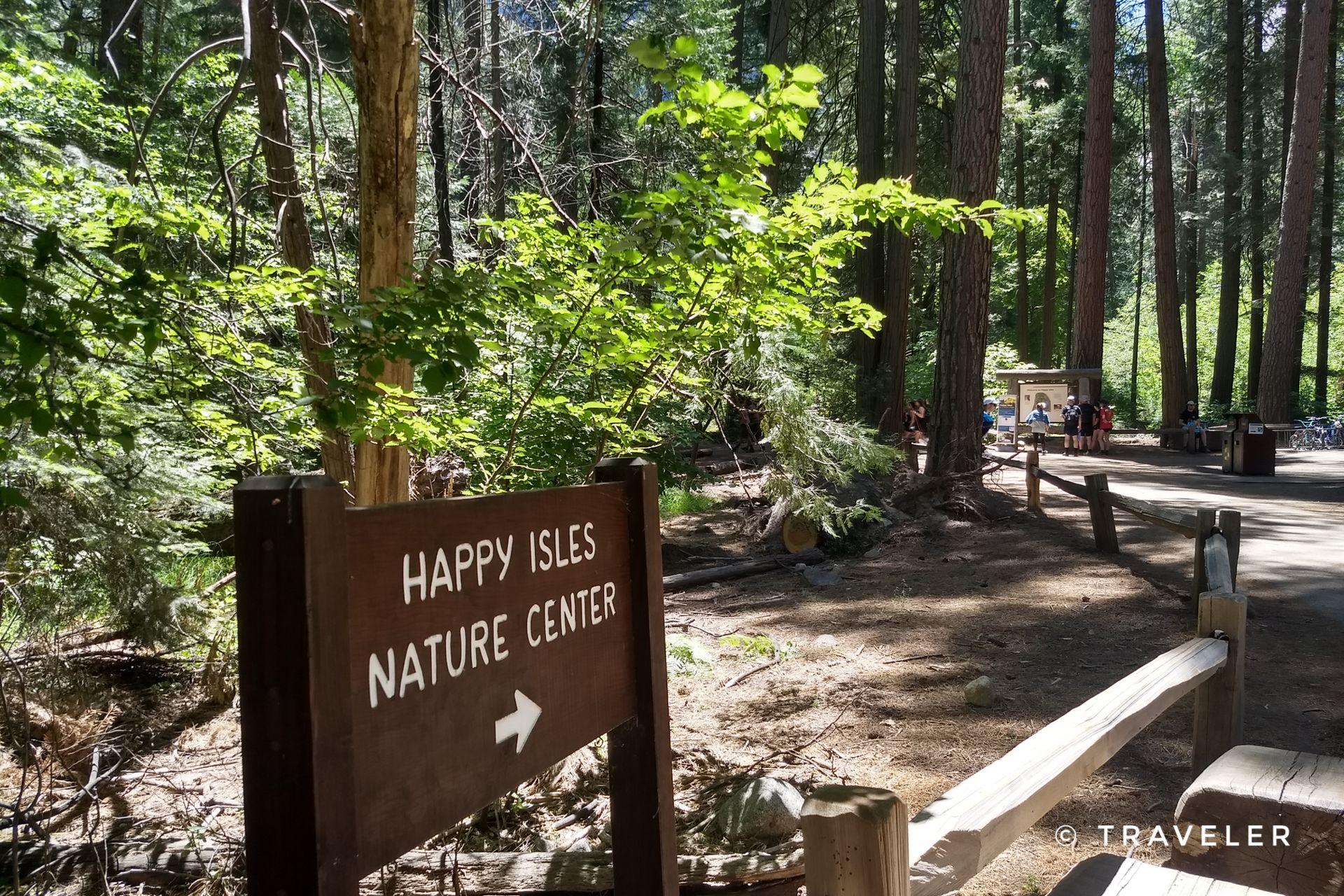 Wooden sign points to a nature center along a sun-dappled forest path.
