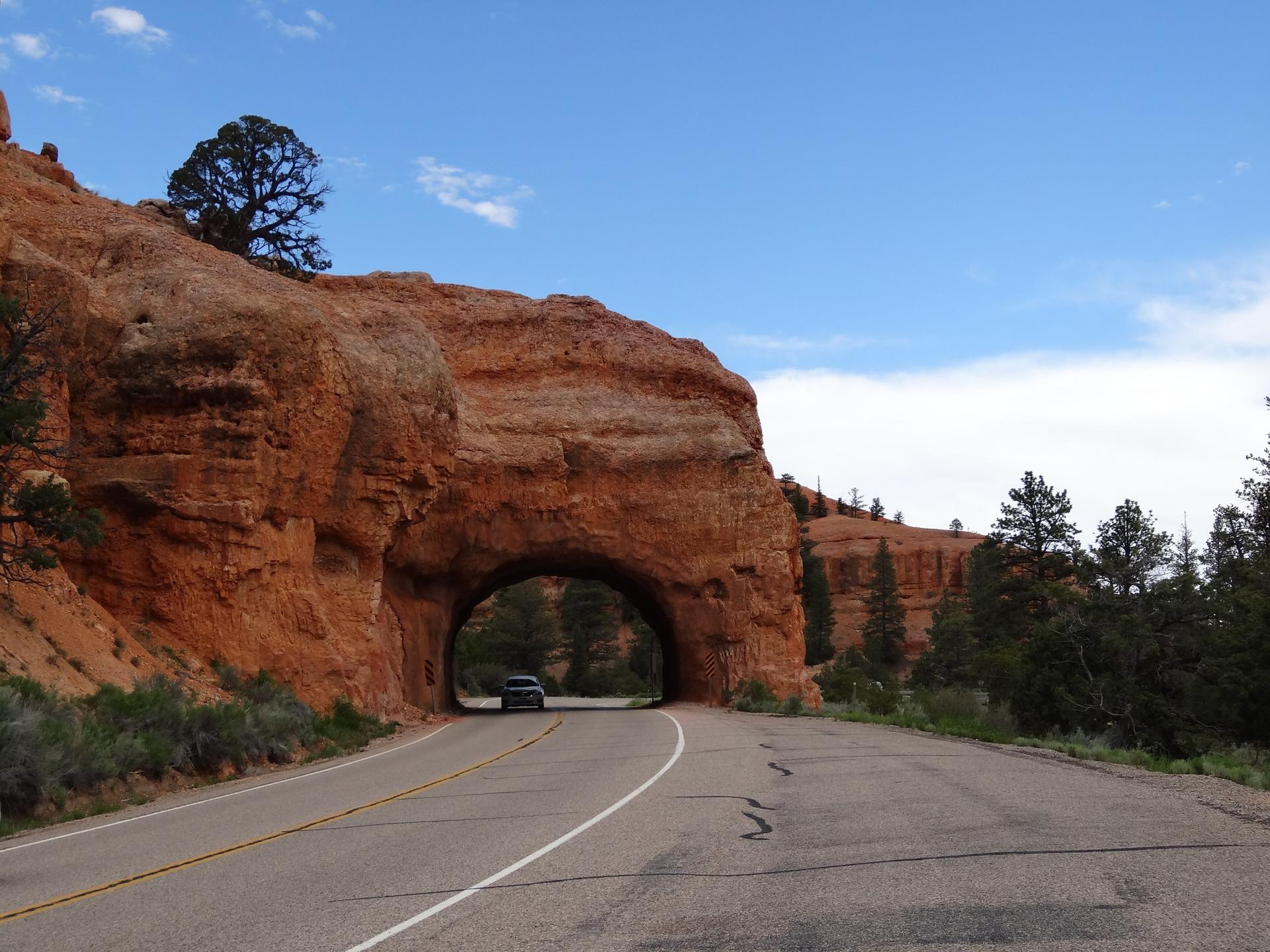 A car approaches a tunnel carved through a large red rock.