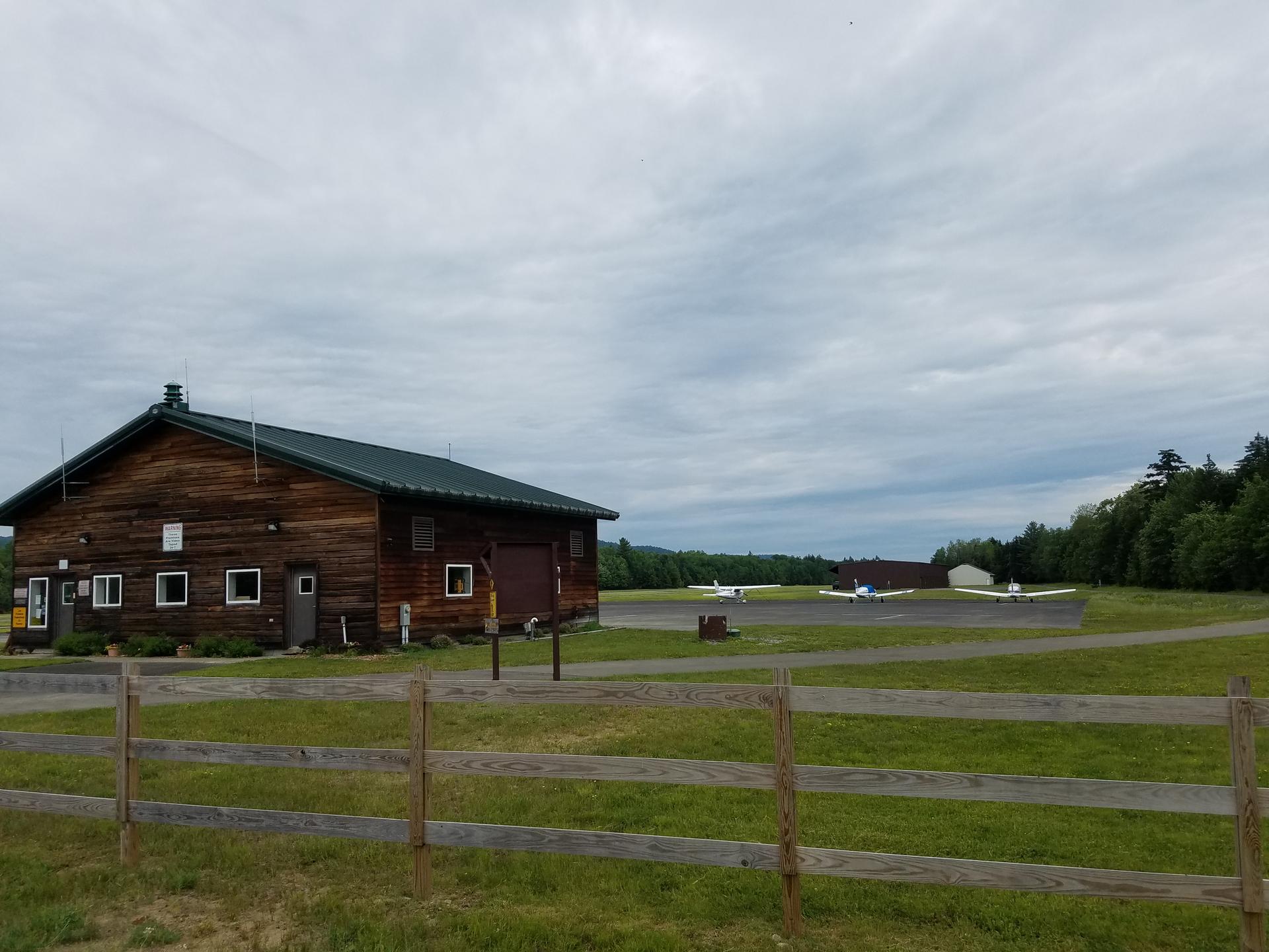 Wooden building next to a small airfield with planes under a cloudy sky.